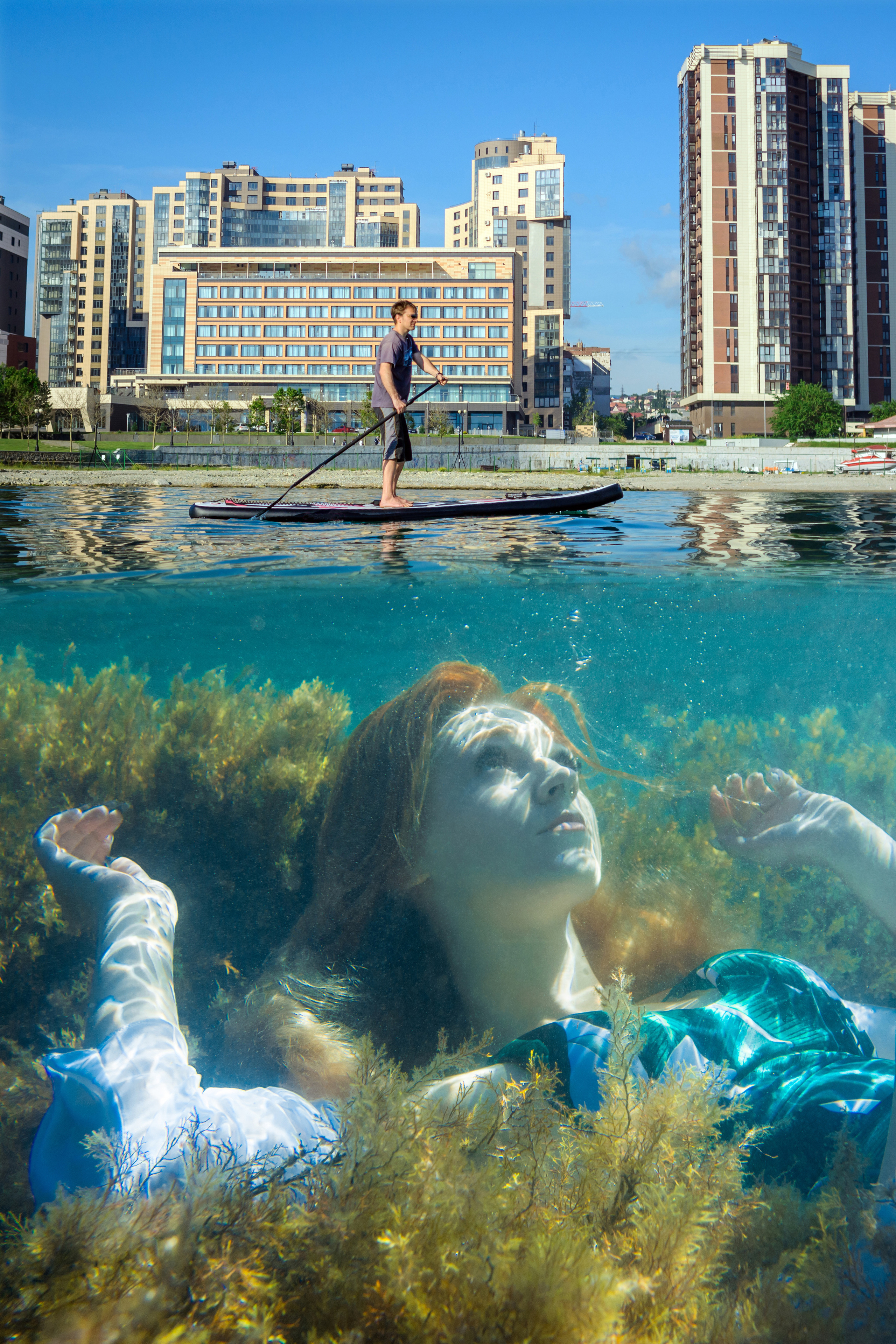 Девушка, лежащая в водорослях под водой и город