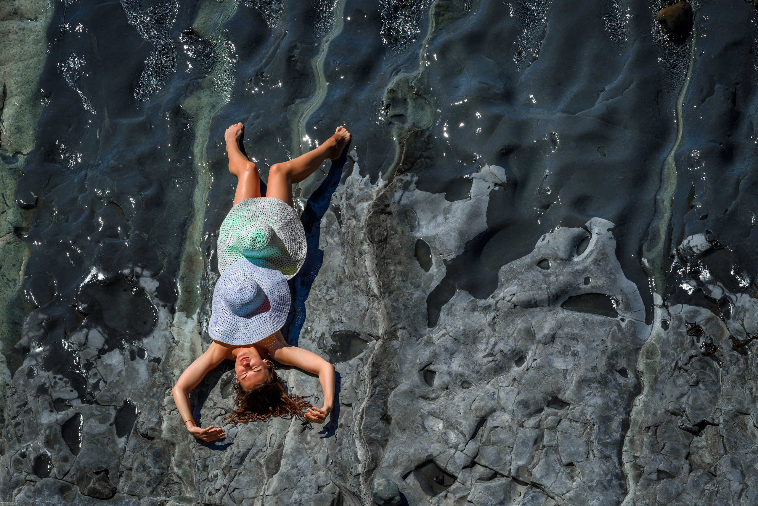 Девушка, прикрытая двумя шляпами, лежит на каменном пляже