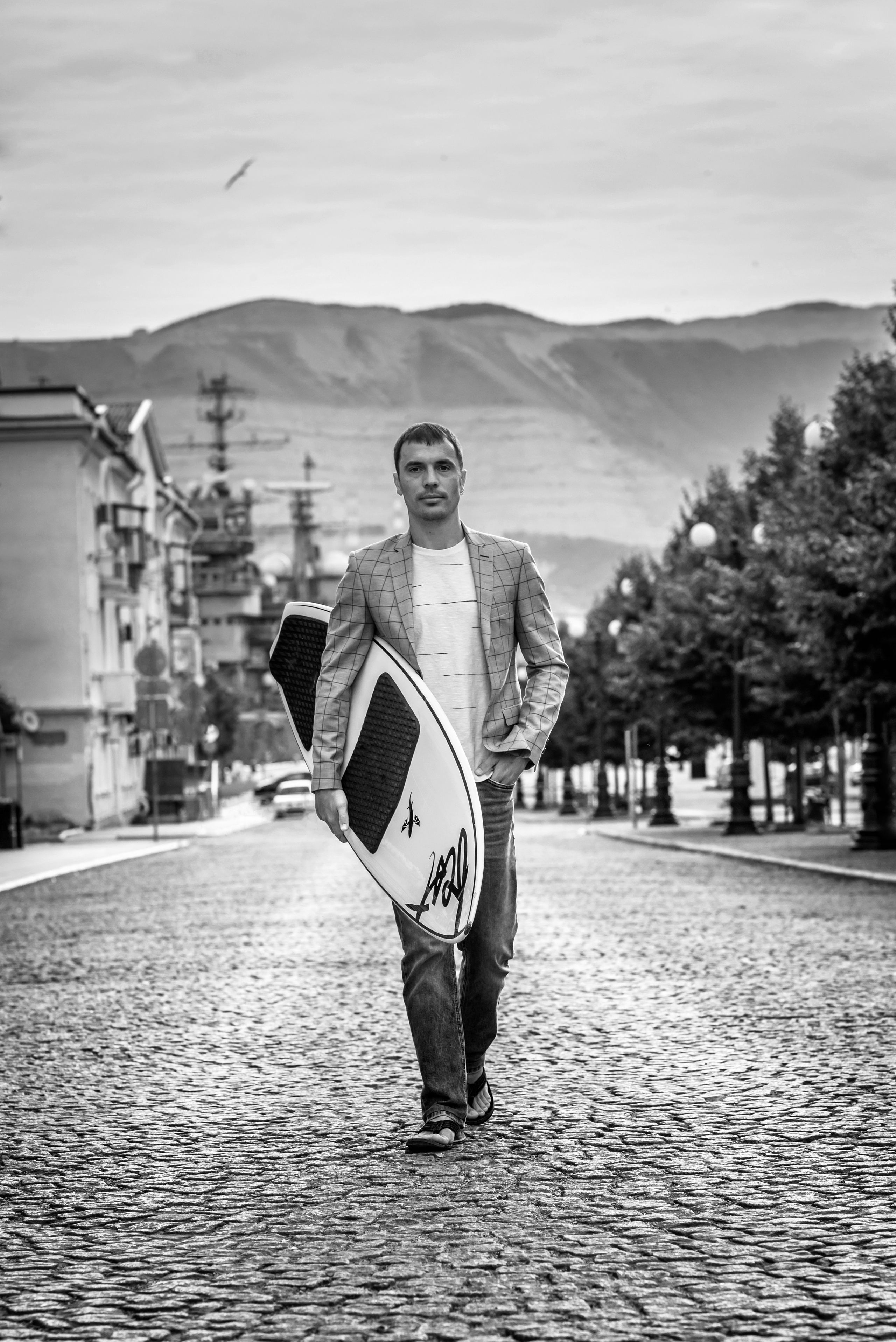 Парень в серф доской, гуляющий по дороге в городе