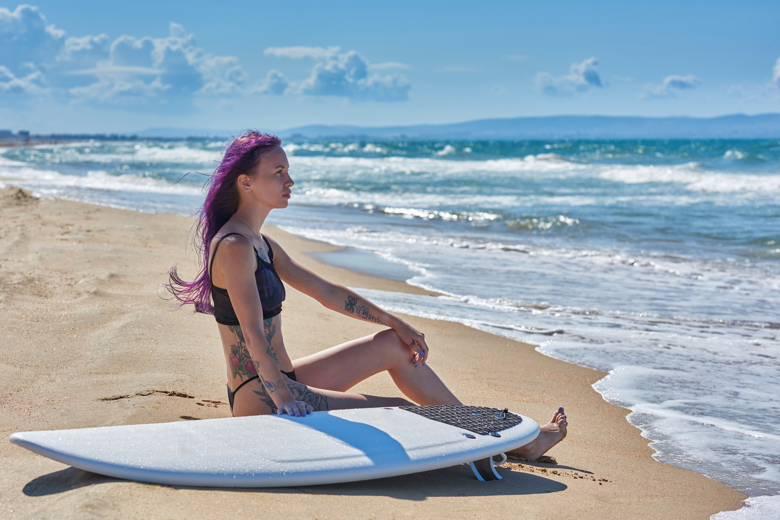 Девушка с серф доской, сидящая на берегу океана