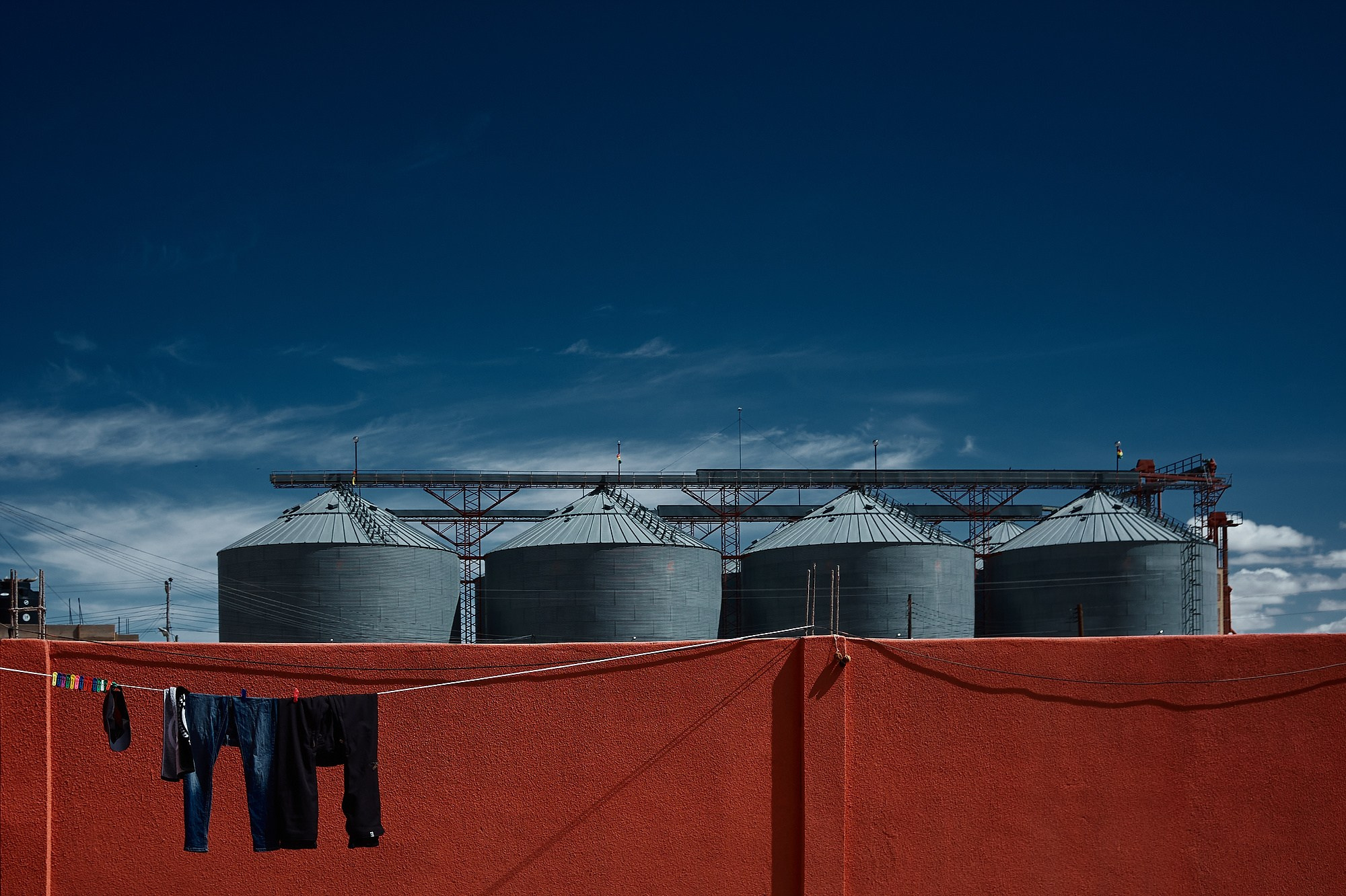 Визуальное исследование городского пространства. Кадр построен на резком контрасте холодного синего неба, стальных индустриальных форм и теплой фактуры оранжевой стены с элементами быта