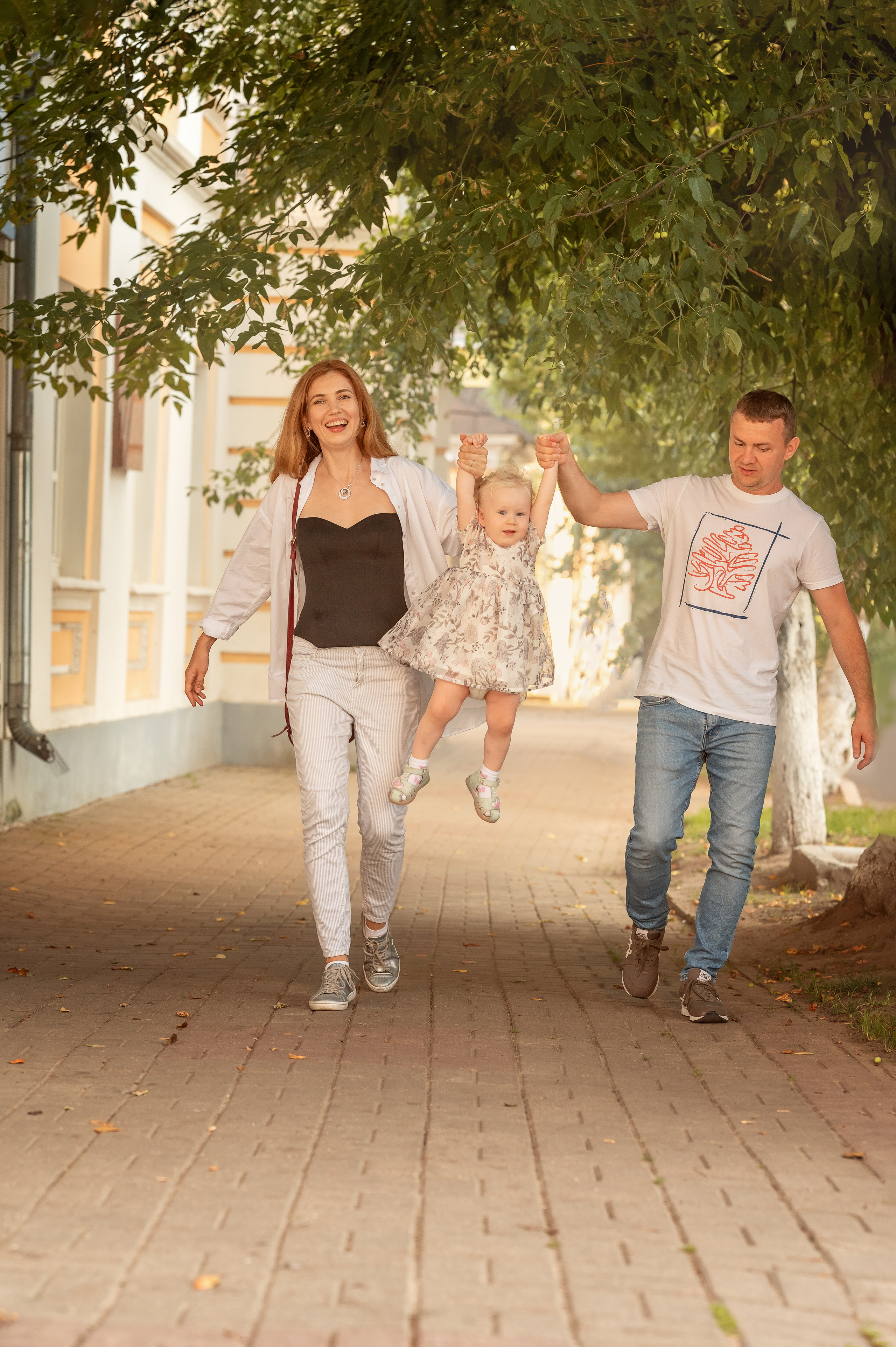Красивые мама и папа гуляют с маленькой дочкой и им весело.