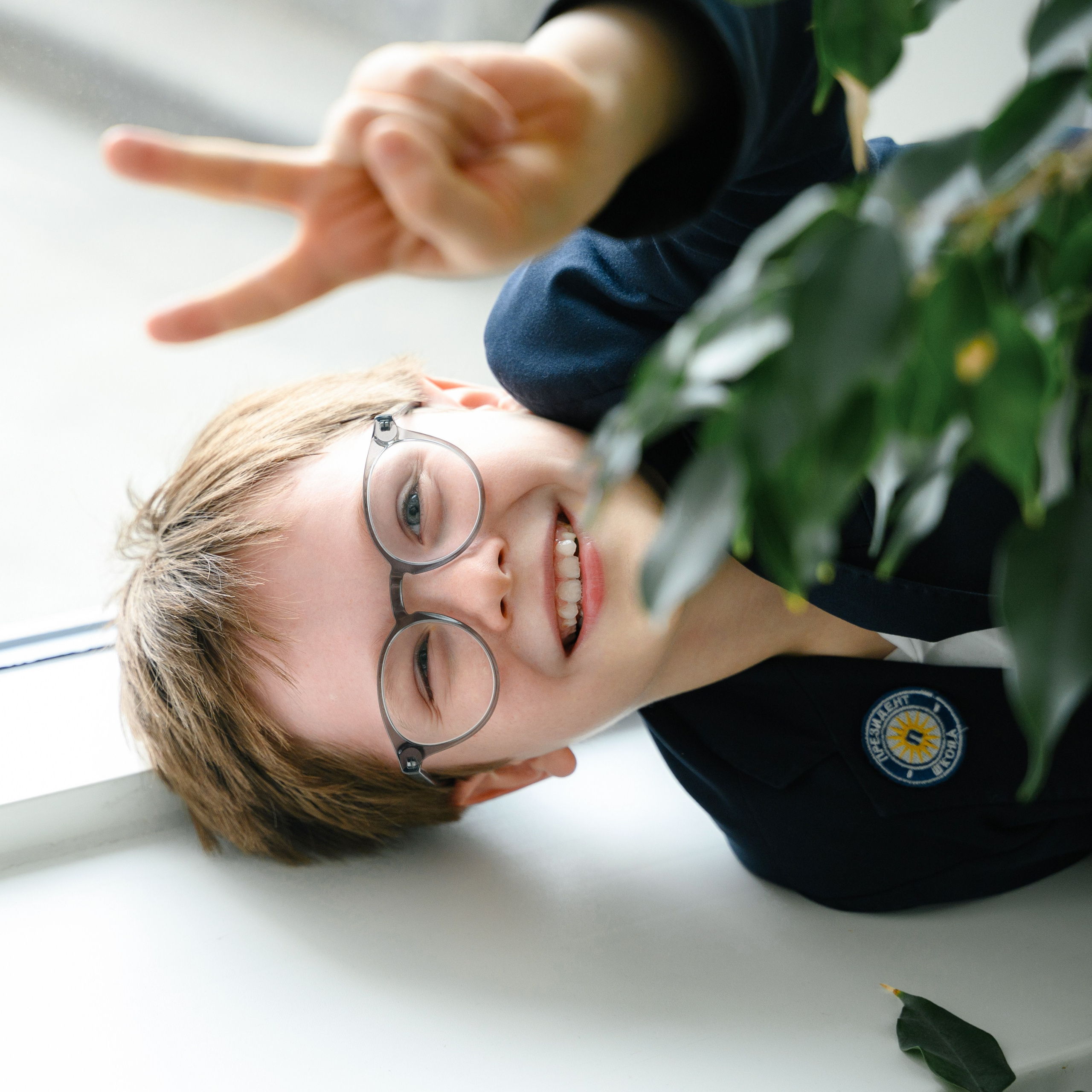 Улыбающийся мальчик в очках выглядывает из за комнатного растения