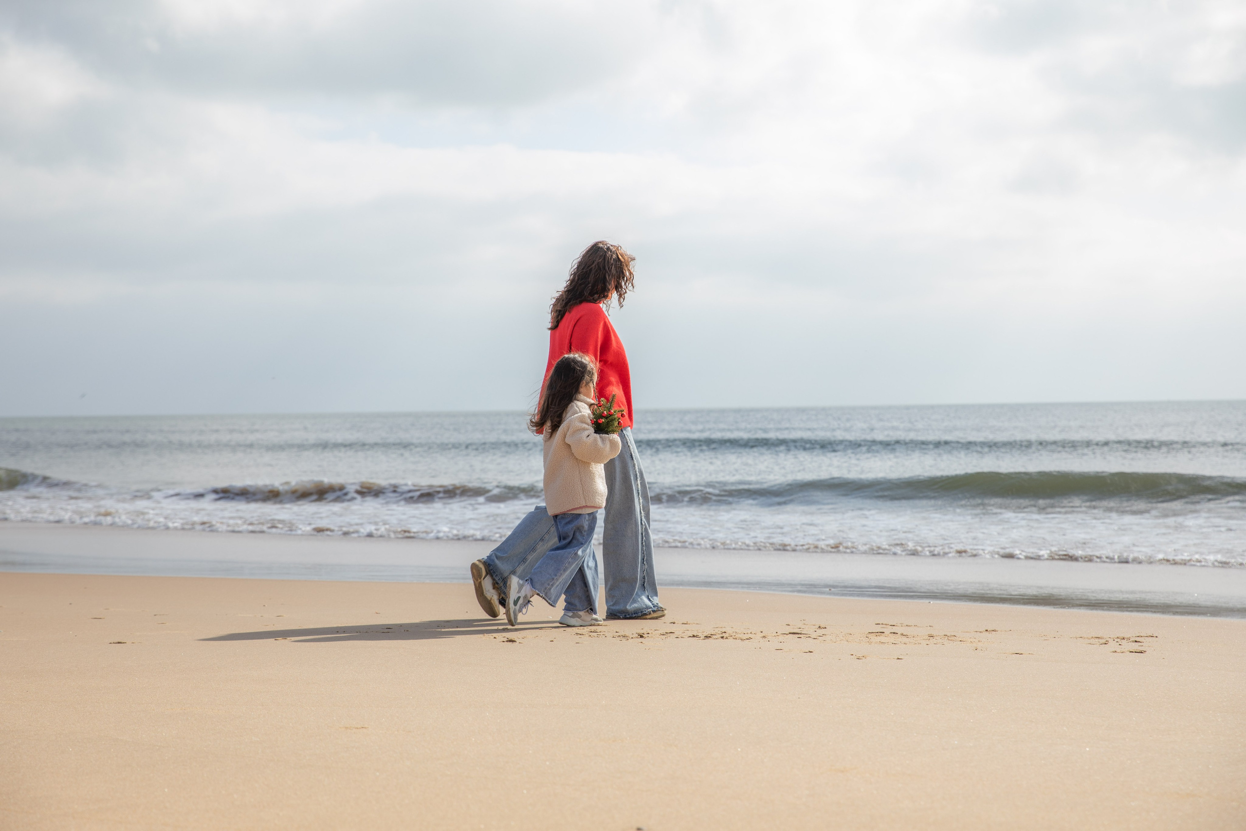 Mum and daughter walking hand in hand, enjoying a peaceful stroll along the beach. Mother and daughter holding hands, their footprints left behind in the soft sand