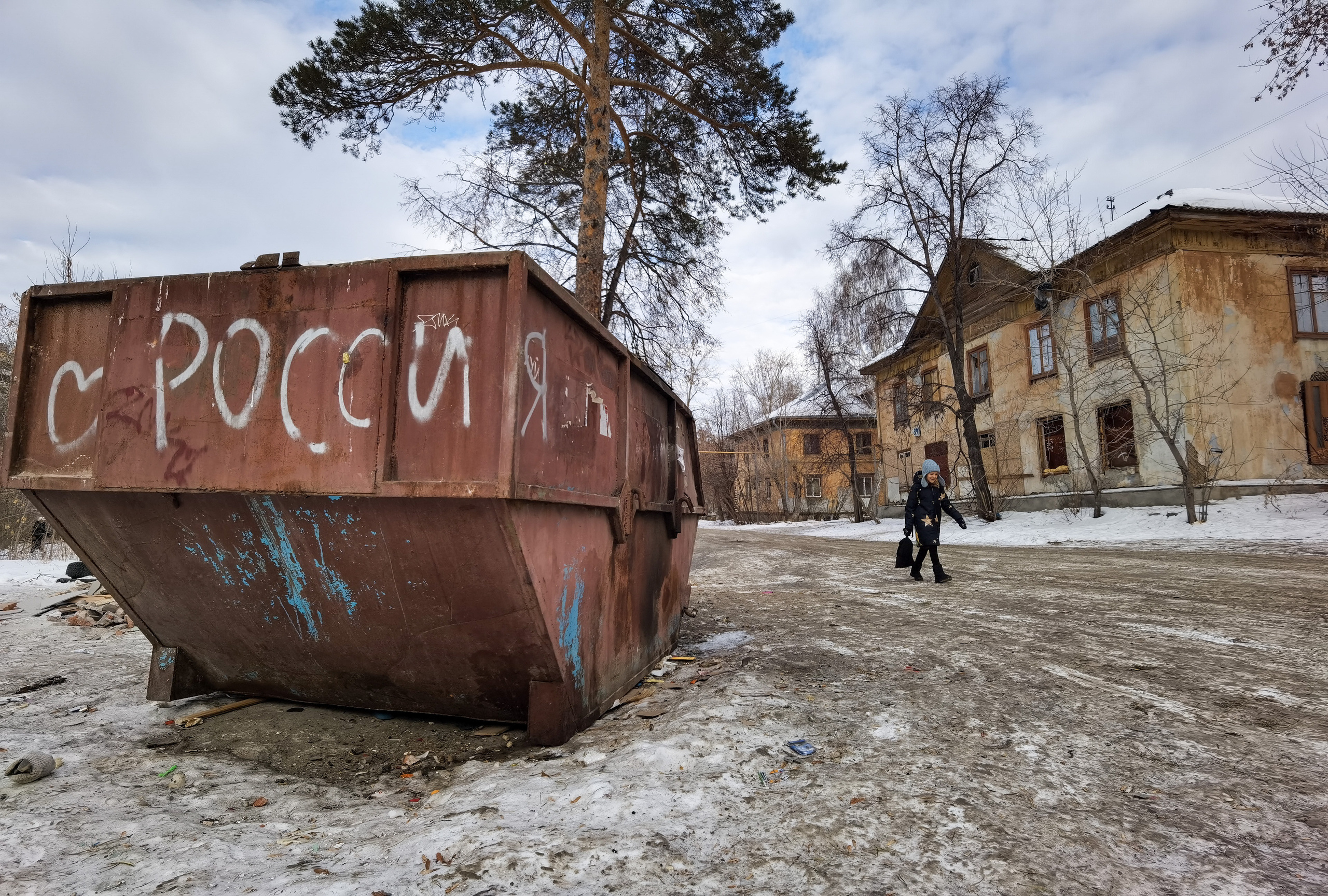 "РОССИЯ" из серии «Новая реальность 2022» Школьница идет мимо огромного мусорного контейнера с надписью «Россия»на задворках района Вторчермет среди заброшенных  домов Екатеринбург, 2022