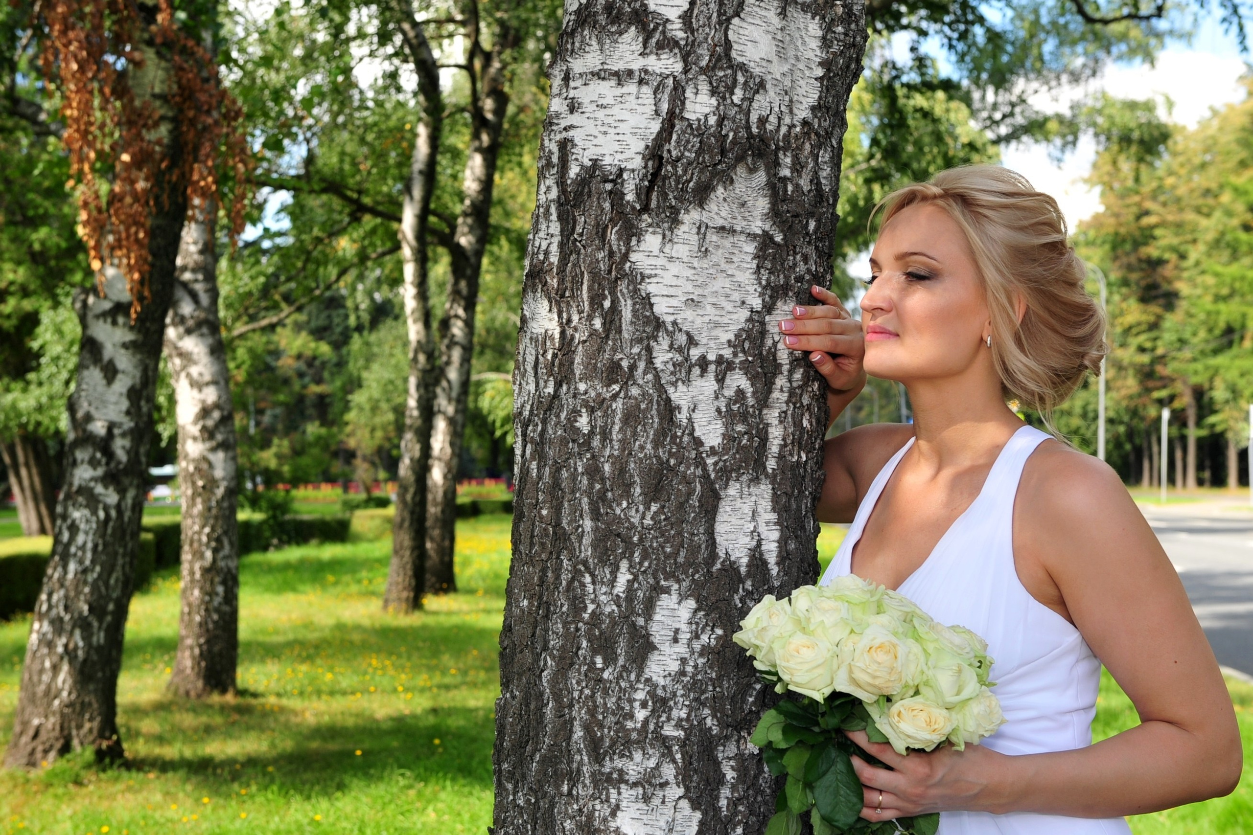 Свадьба на Воробьёвых Горах рядом с МГУ, невеста стоит, облокотившись на берёзку в берёзовой роще рядом с МГУ, в руках невеста держит свадебный букет из кремовых роз