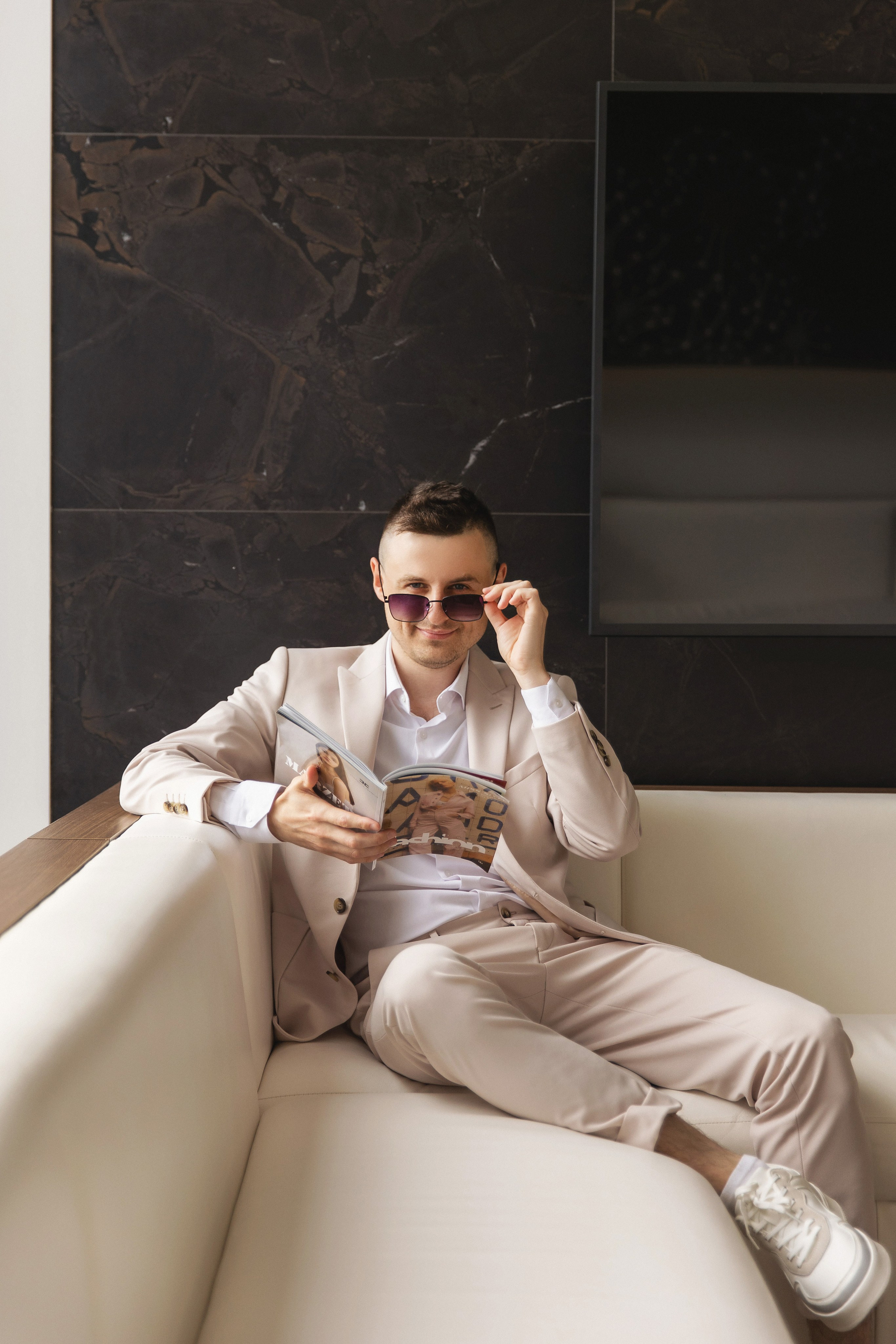 Парень сидит на белом диване и держится за очки