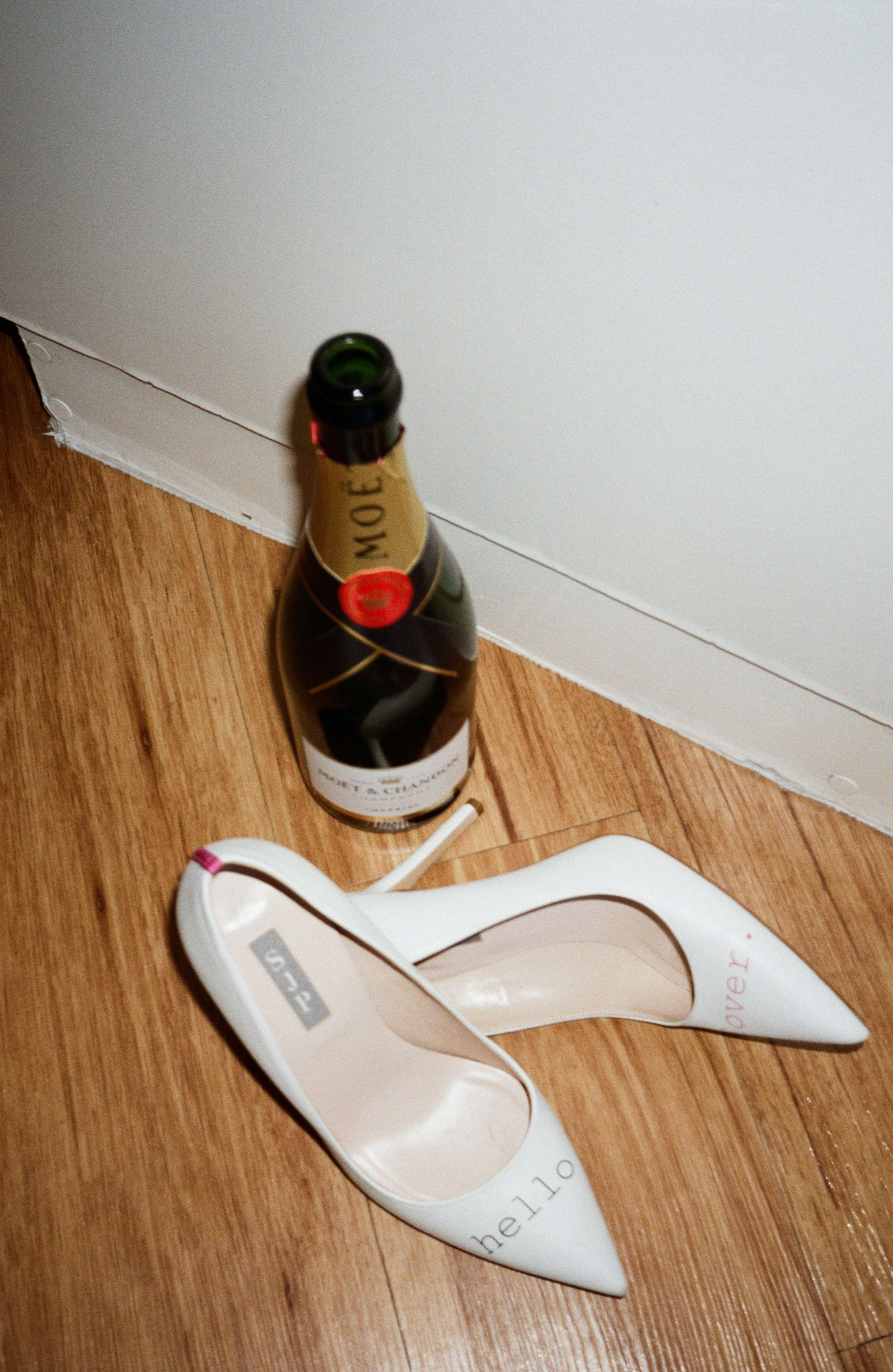 a detailed film photo of an empty bottle of champagne and high heel white shoes