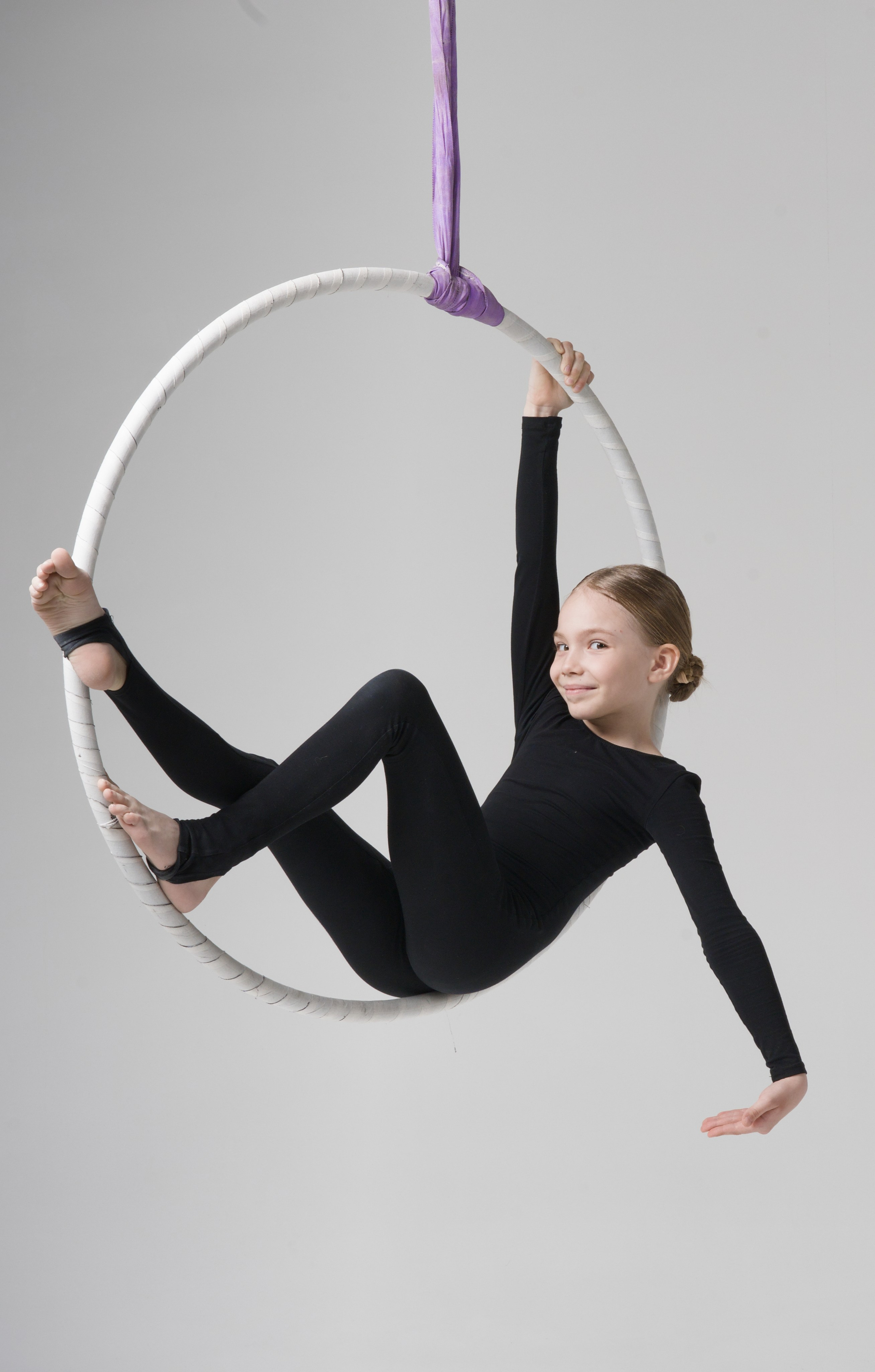 Эстетичный портрет ребенка на воздушном кольце, демонстрация баланса и гибкости на белом фоне