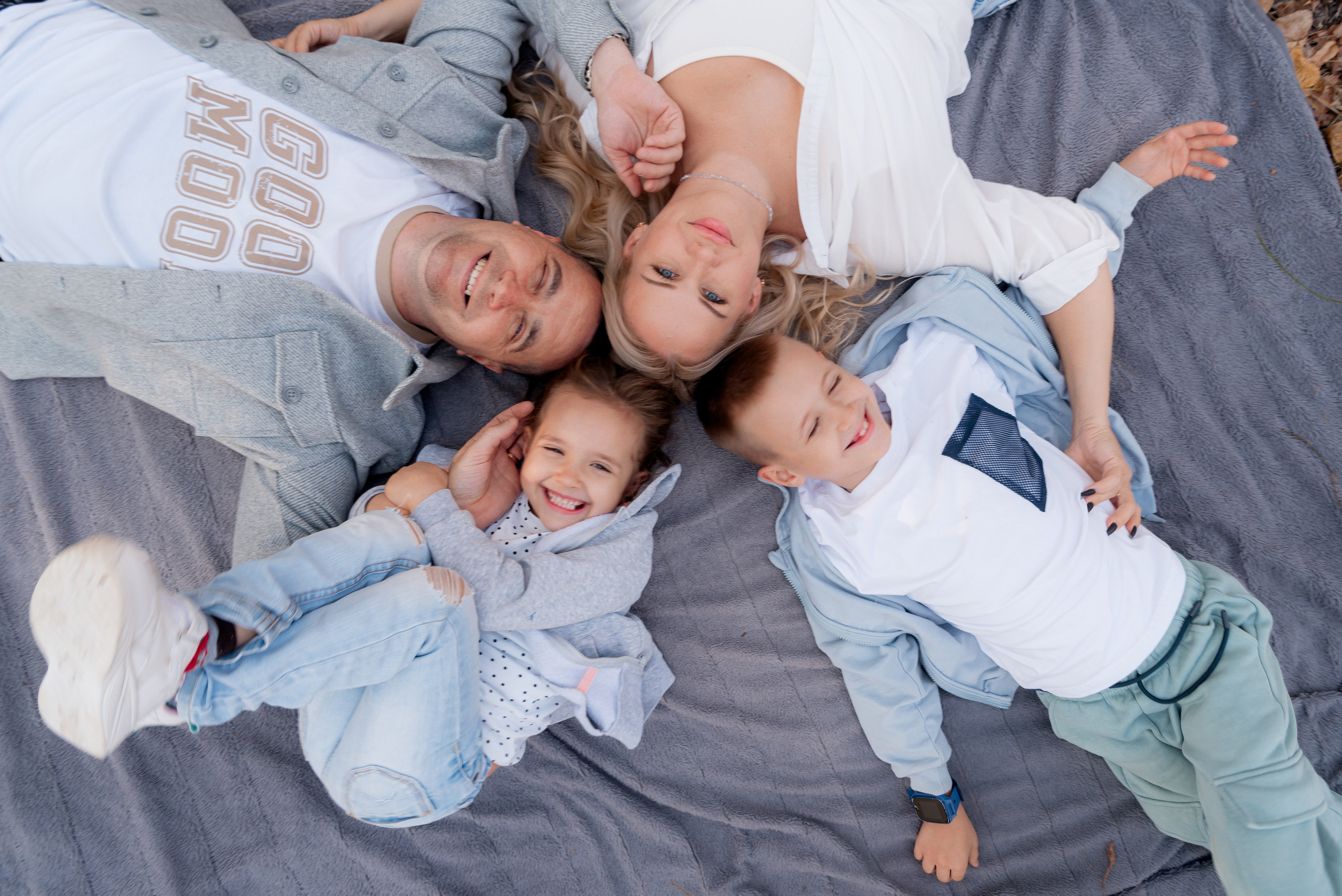 Семейная фотосессия в парке Волгограда - мама, папа, сын и дочка смеются вместе на одеяле.