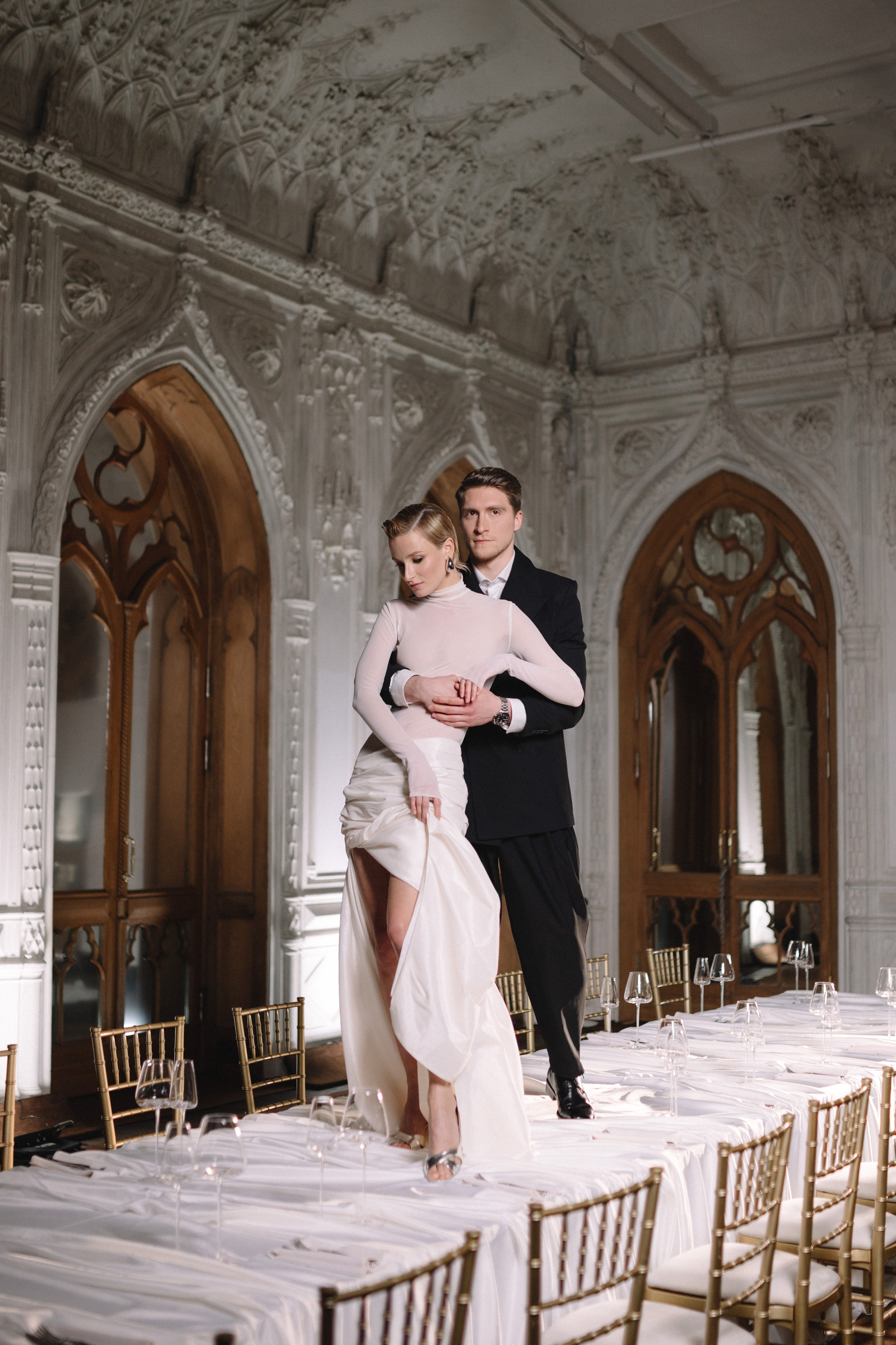 Восторженные взгляды зрителей направлены на пару, появившуюся в центральном проходе, наполняя сцену радостью и гармонией.