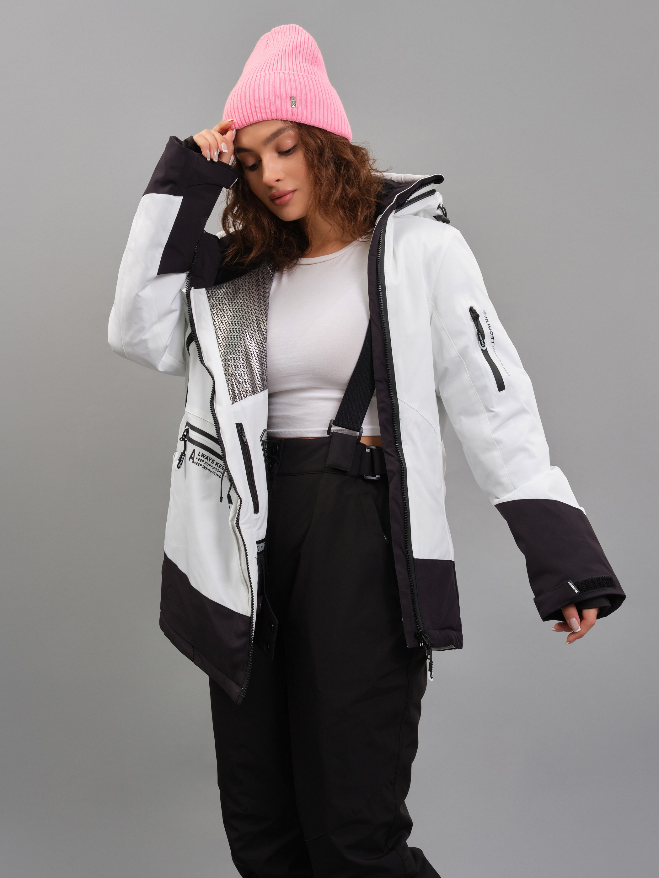 Женщина в светлой зимней лыжной куртке и розовой шапке