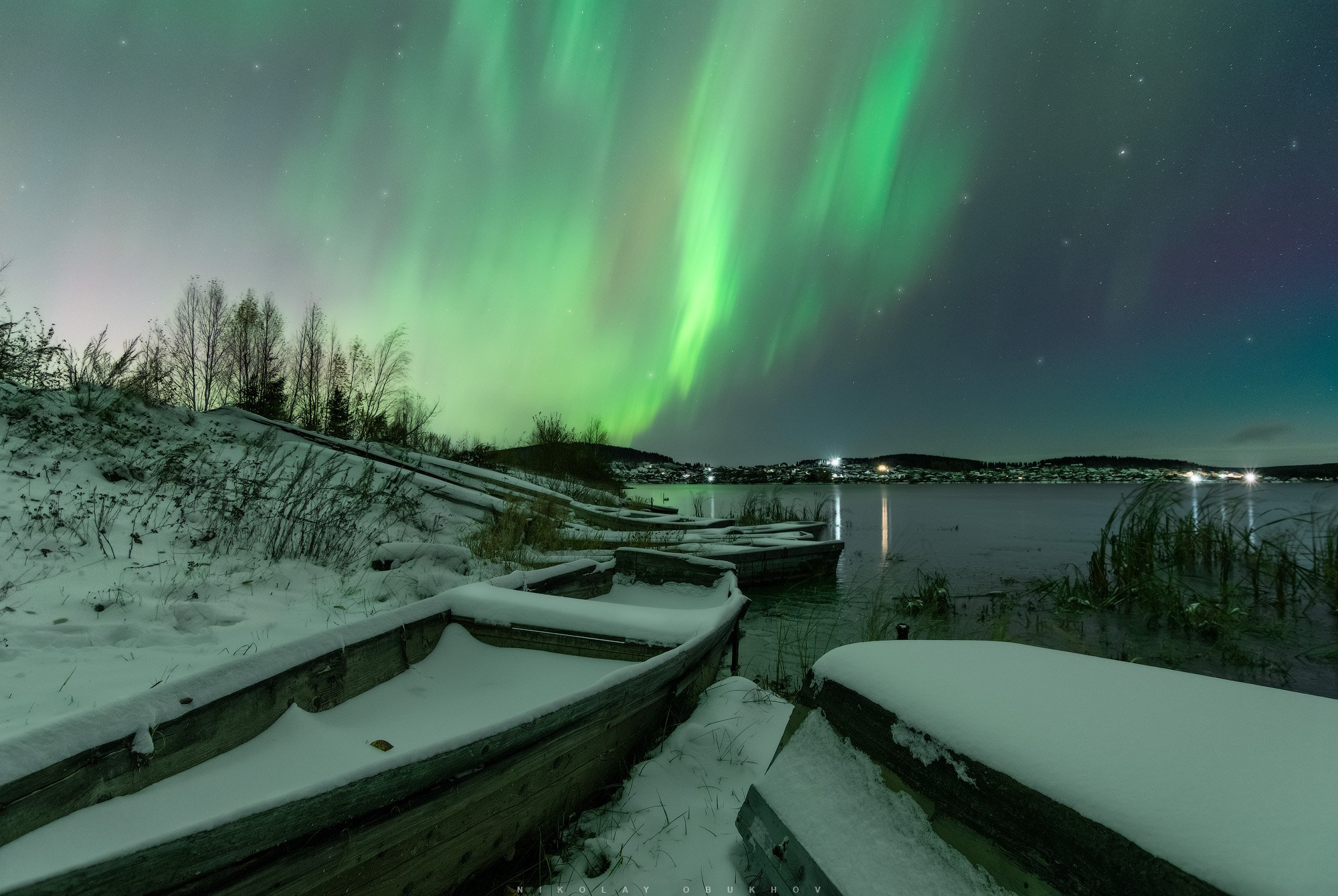 Заснеженные лодки на берегу пруда и северное сияние в Черноисточинске вблизи города Нижний Тагил.