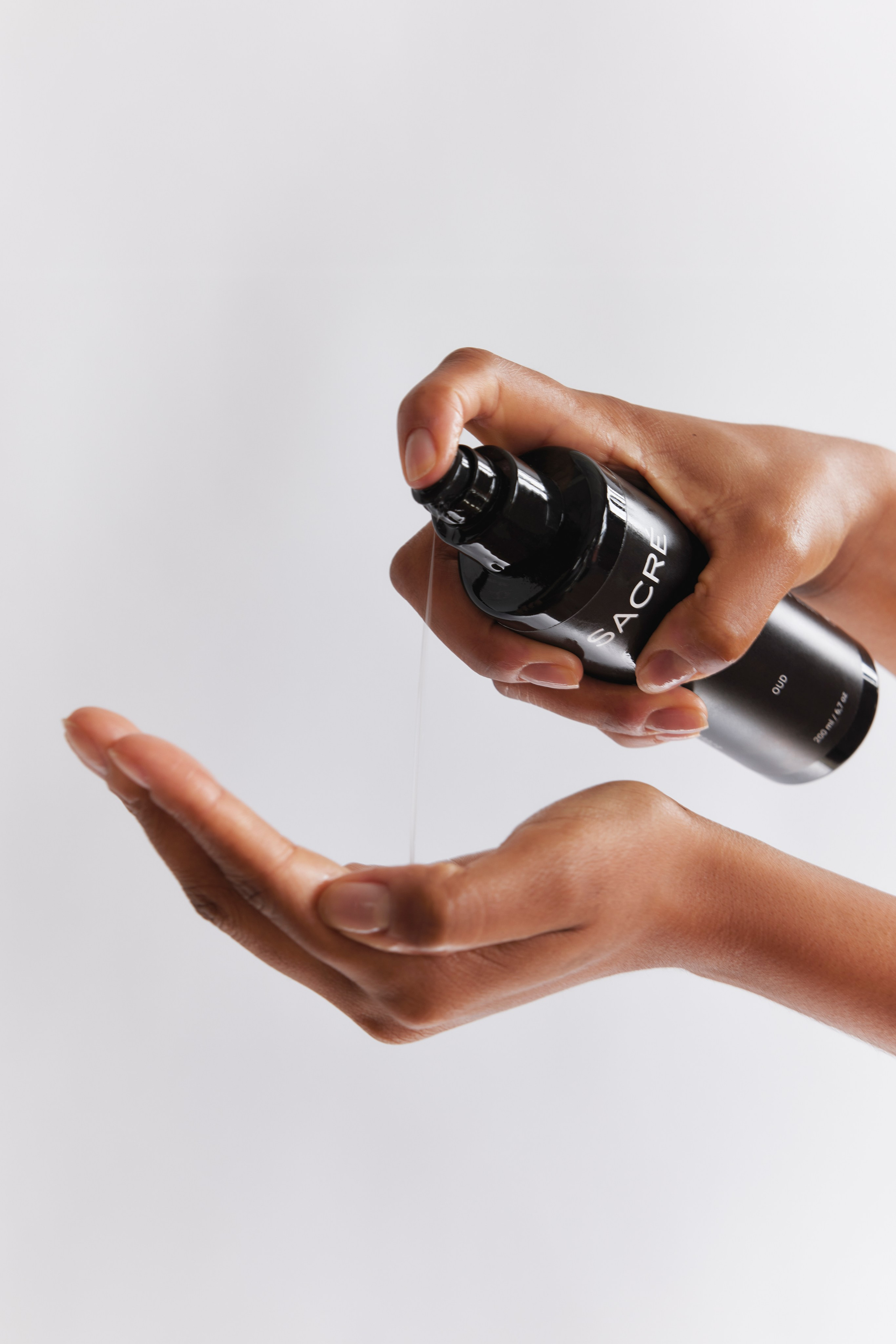 Model applying serum from a black bottle, showcasing high-end skincare application.