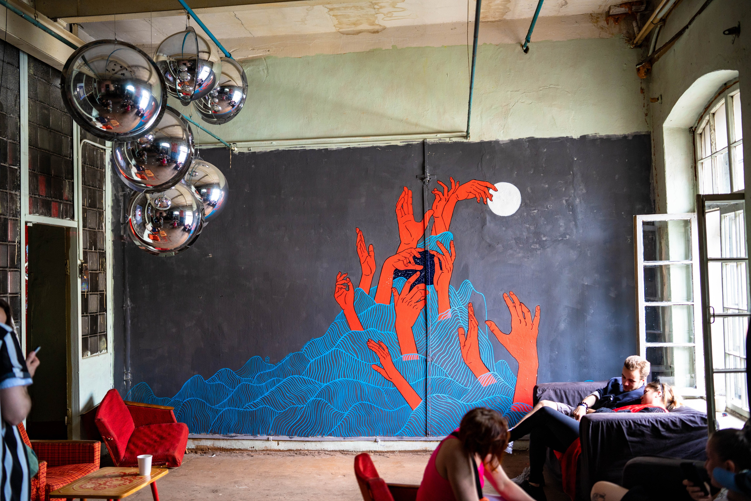 На серой стене изображены музыкальные волны и красно-оранжевые танцующие руки.