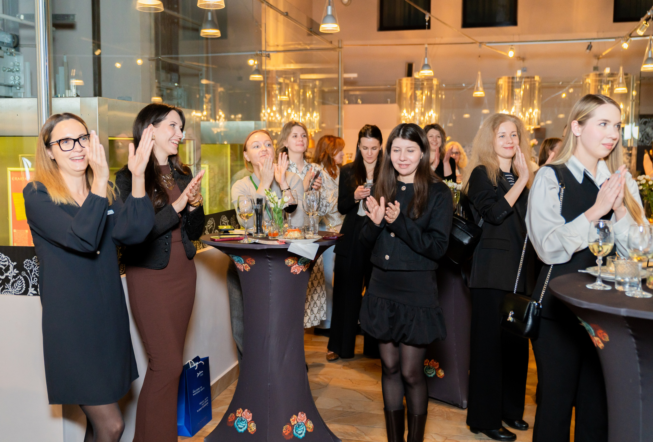 Гости аплодируют на мероприятии в Radisson Sonya. Группа женщин в деловой одежде радостно хлопает в ладоши. Фотография Евгения Мальцева.
