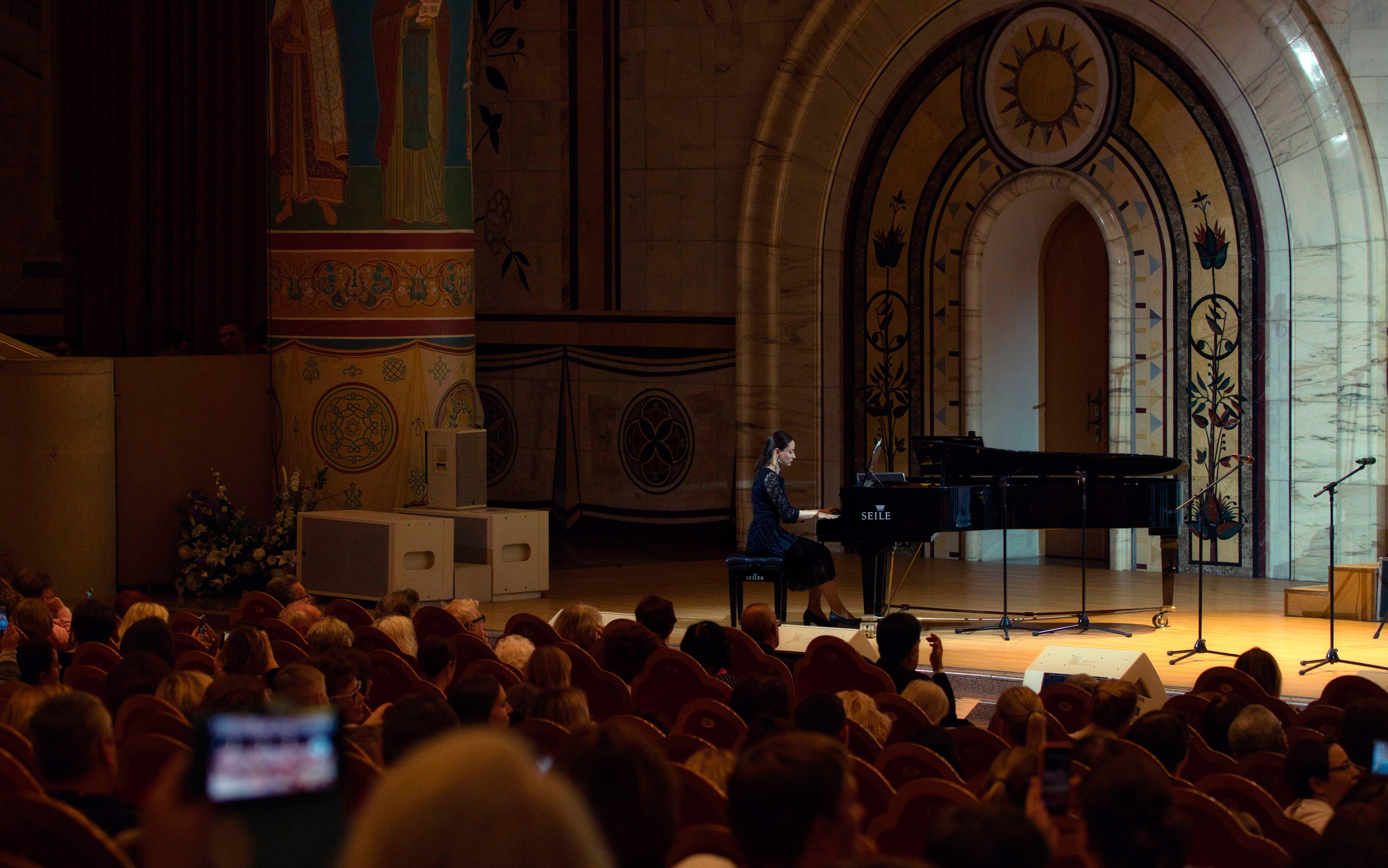 Пианистка играет на рояле Seiler в красивом концертном зале с декоративными арками и росписью, зрители в зале, классическая музыка, профессиональная концертная съемка