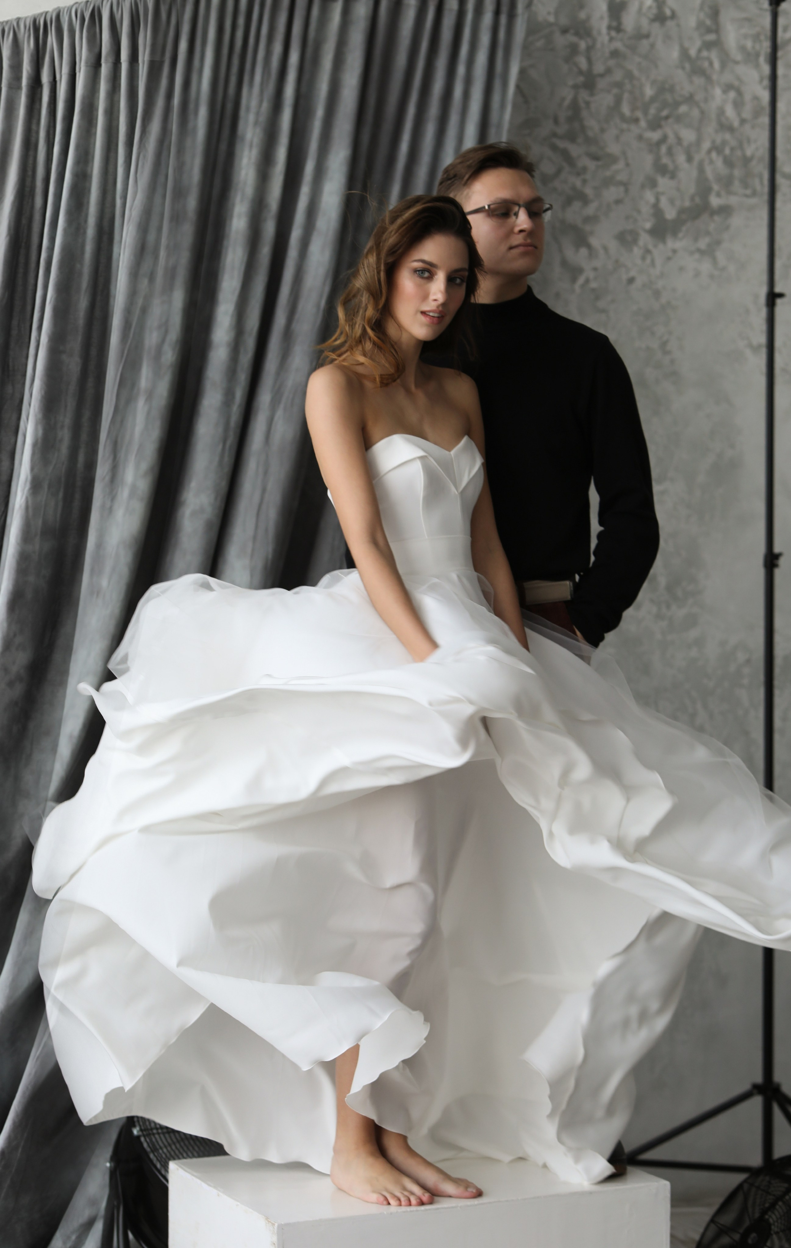 Свадебные фотографии жениха невеста стоят на подиуме снизу вентилятора разливают платье