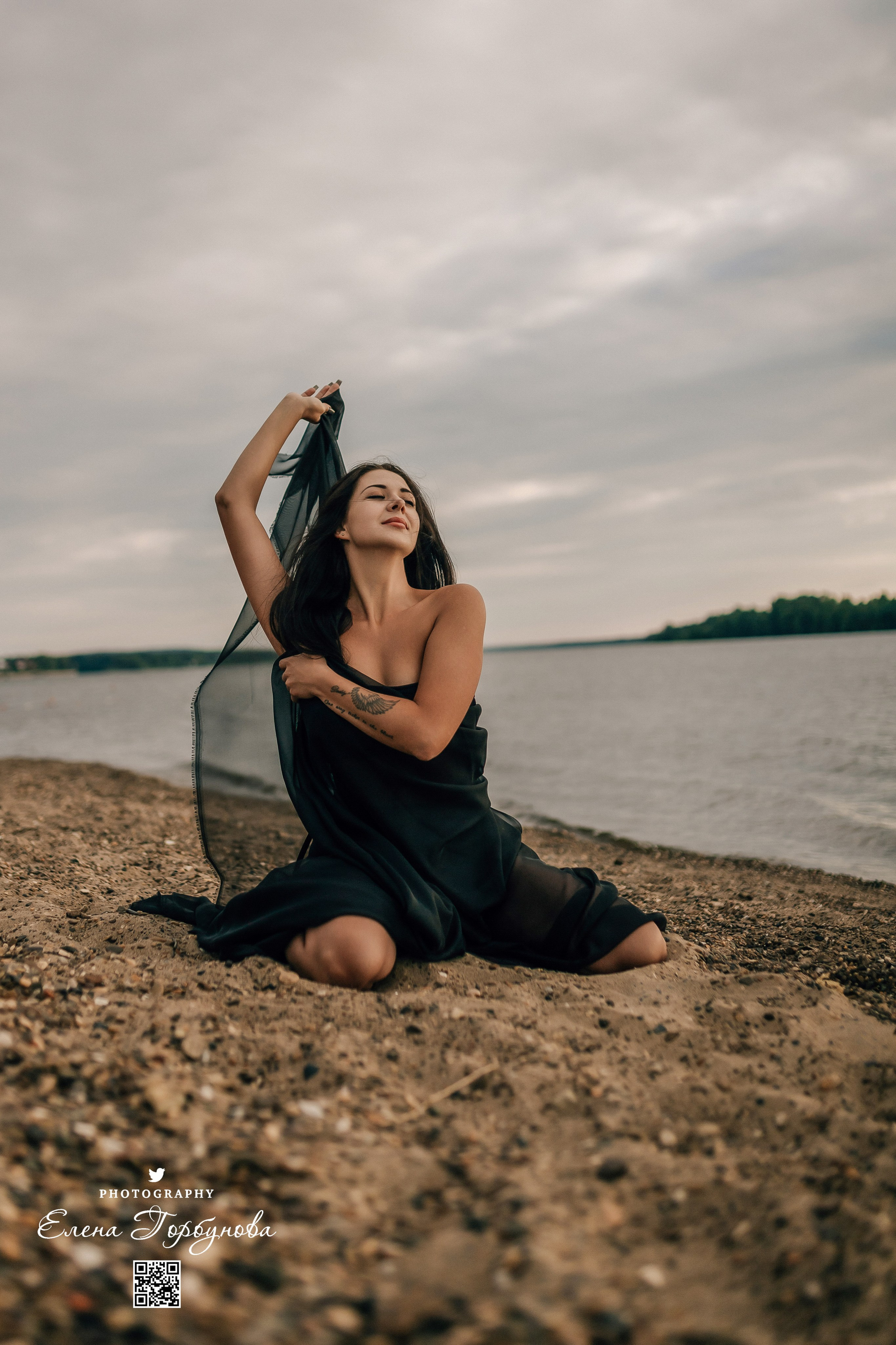 Фотосессия с черной тканью. Легкая черная вуаль летит на вертру. Фотосессия у реки черная серия с тканью. Девушка укуталась в черную ткань. Прогулка по набережной. Песок, речка, модель в черном. Качели над водой, Закат. Девушка лежит на песке. В зеленых деревьях