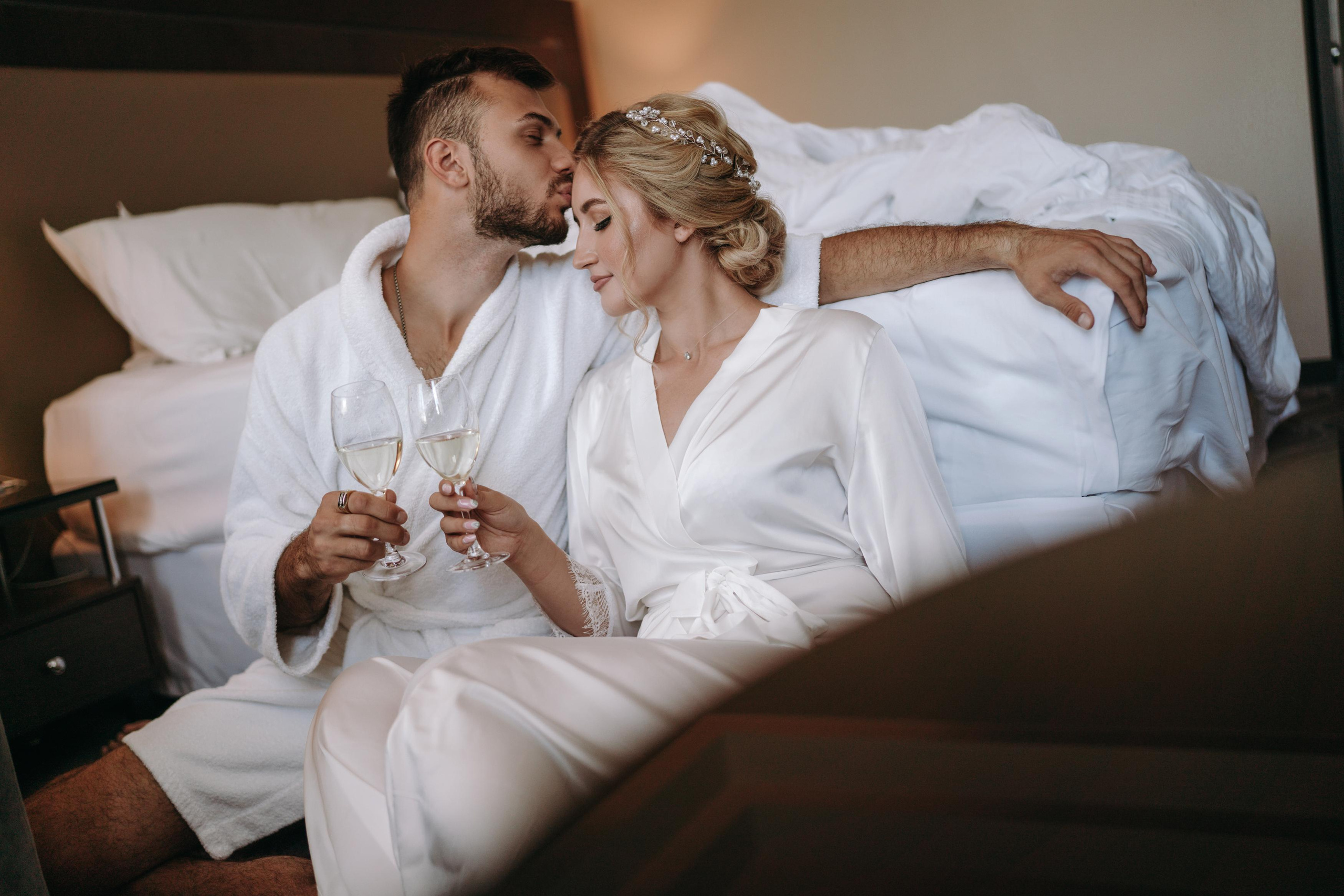 Жених целует невесту сидя на полу в отеле, сборы жениха и невесты