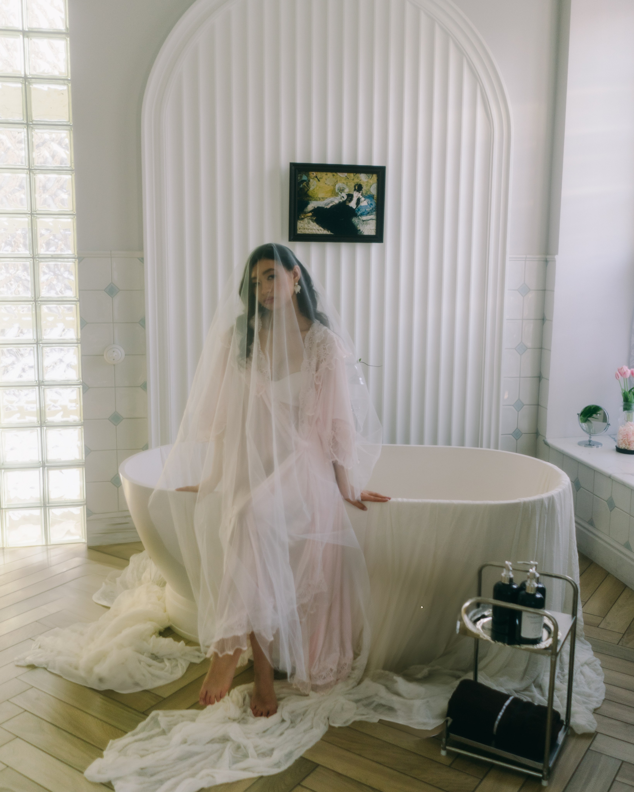 Стильная съемка утра невесты в будуарном стиле: невеста в винтажном пеньюаре и фате сидит на красивой ванне