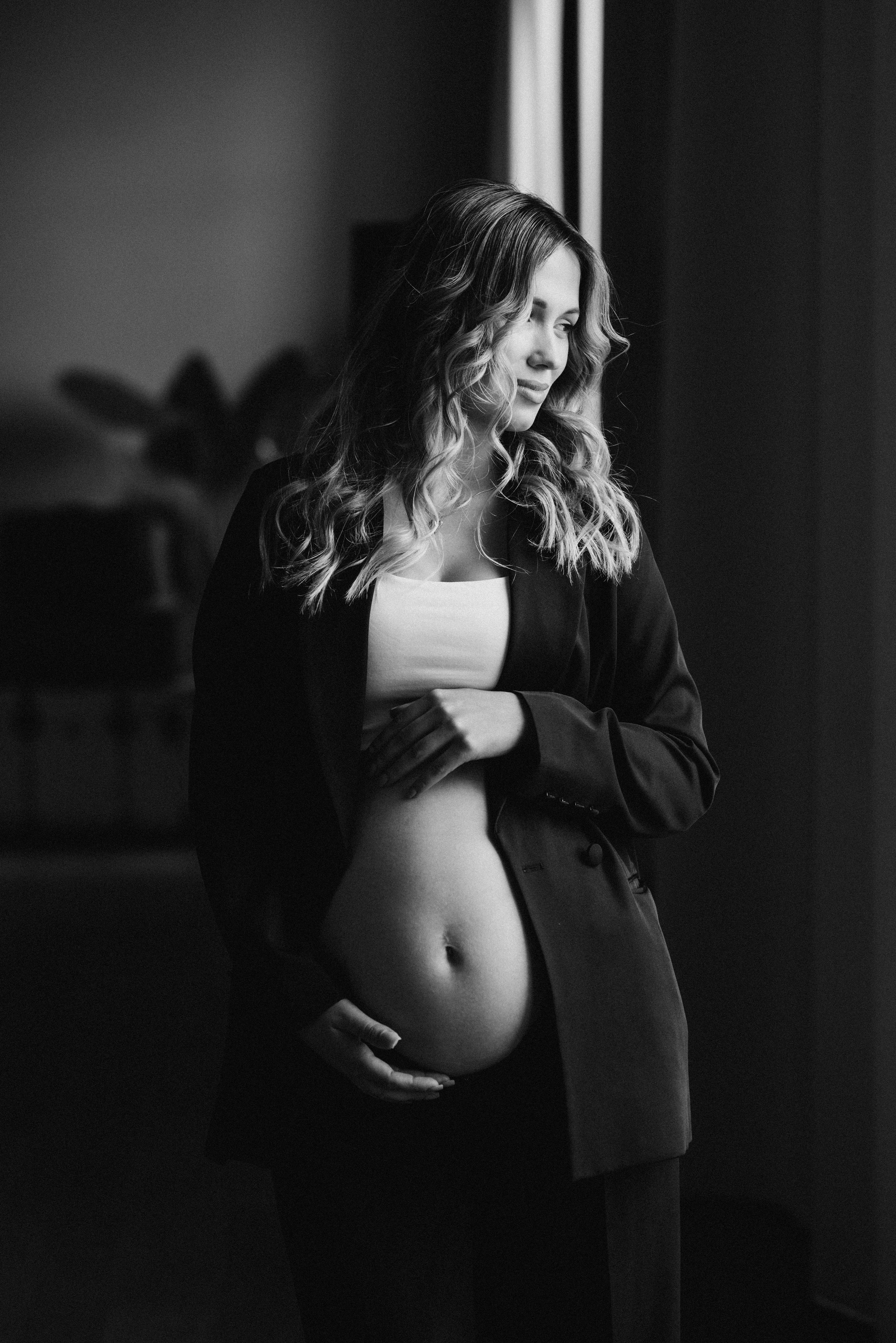 фотосессия для беременных в студии москва — девушка смотрит в окно и обнимает свой животик