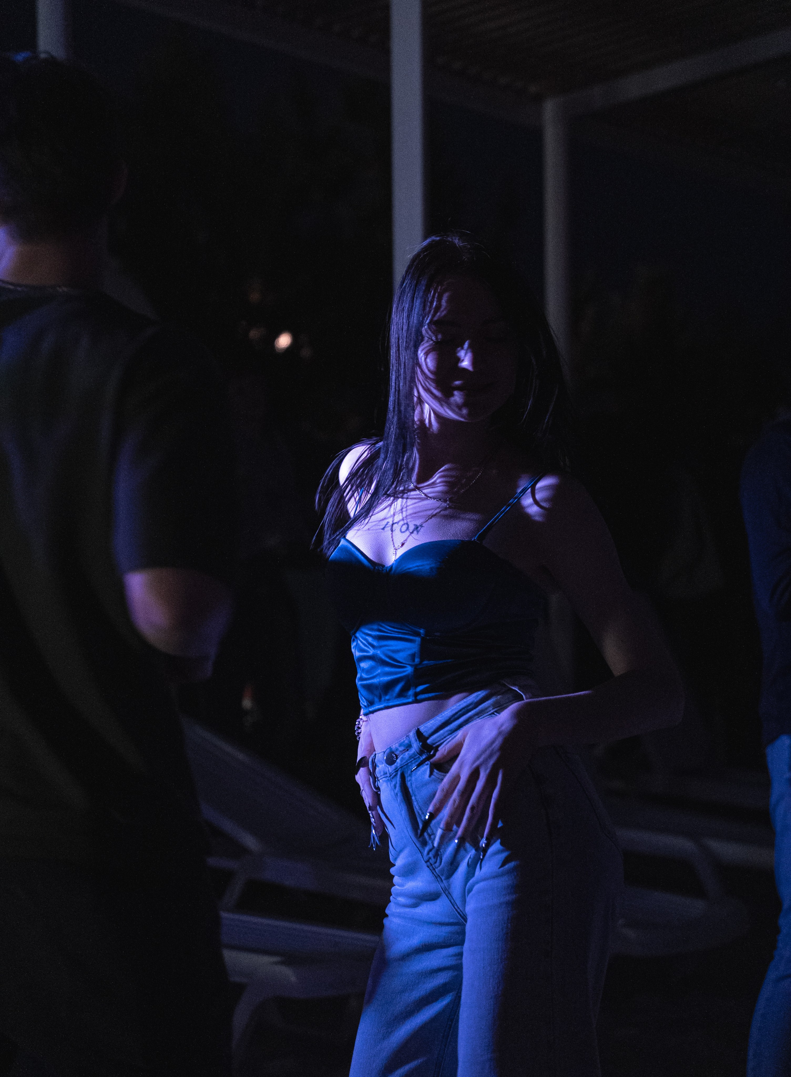 Девушка позирует ночью под фиолетовым светом, на заднем плане — лежаки и деревья