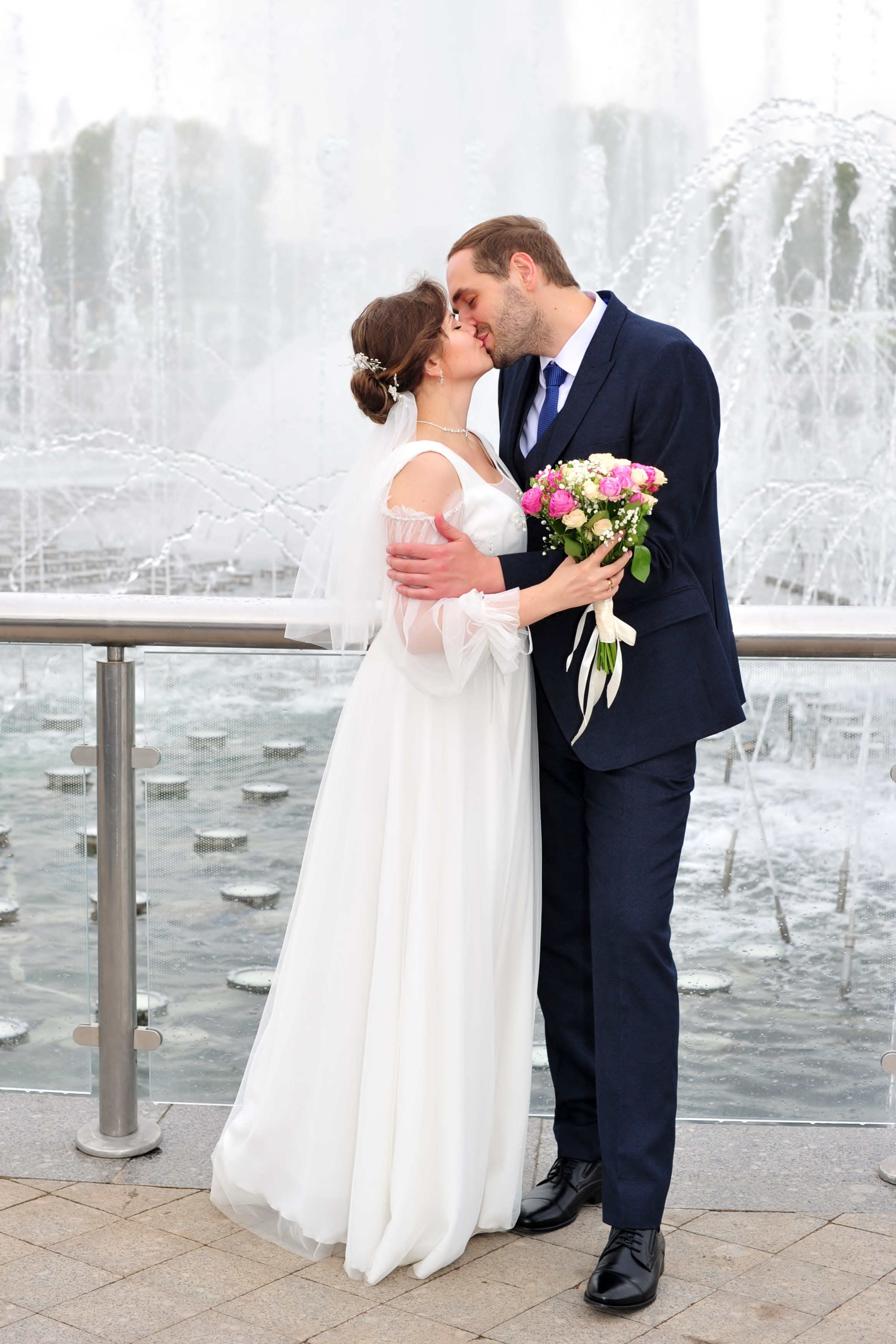 Свадьба в Царицыно пасмурным летним днем, поцелуй новобрачных на фоне фонтана и струй воды 