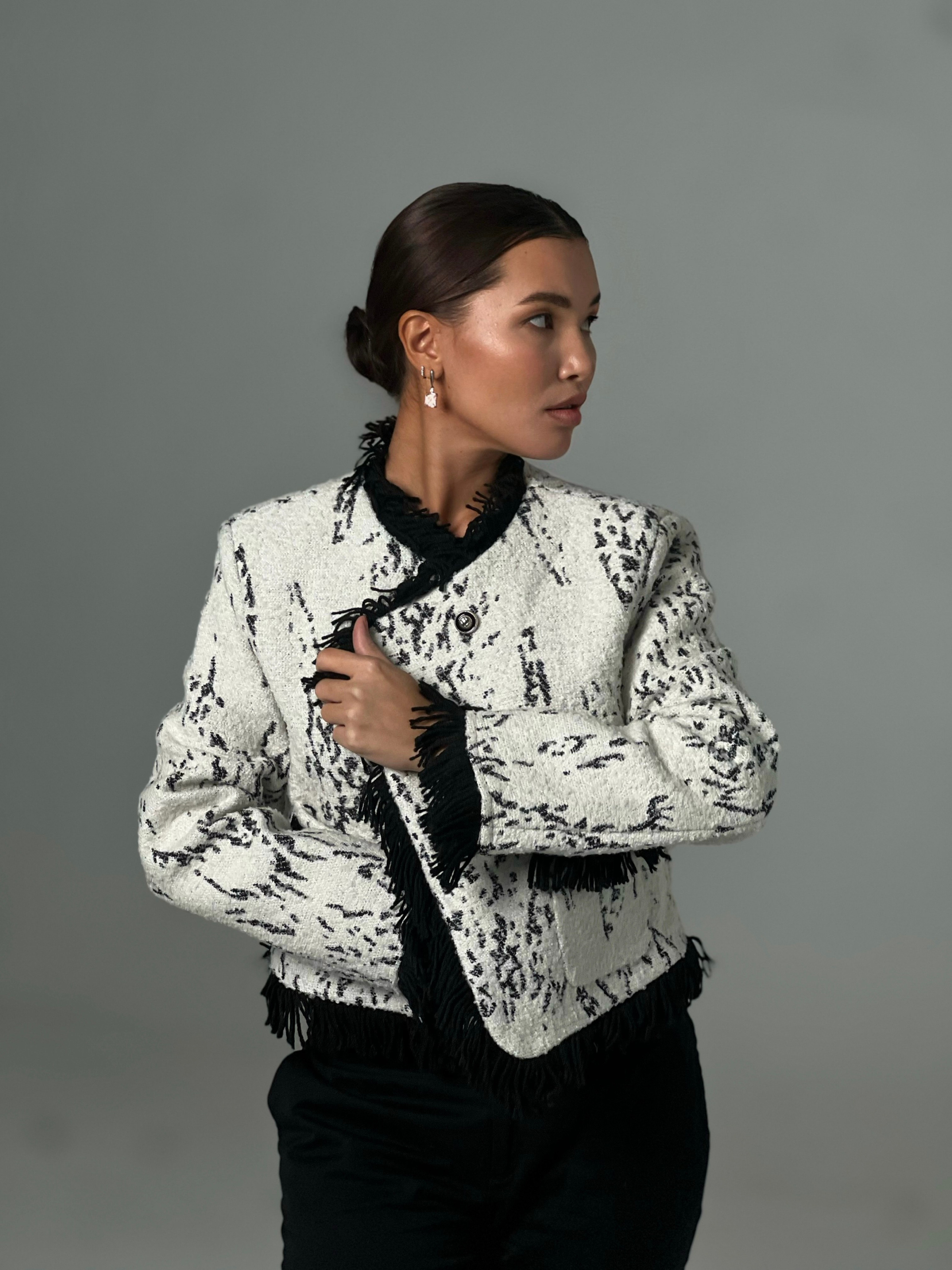 Девушка азиатской внешности позирует в светлом жакете на сером фоне