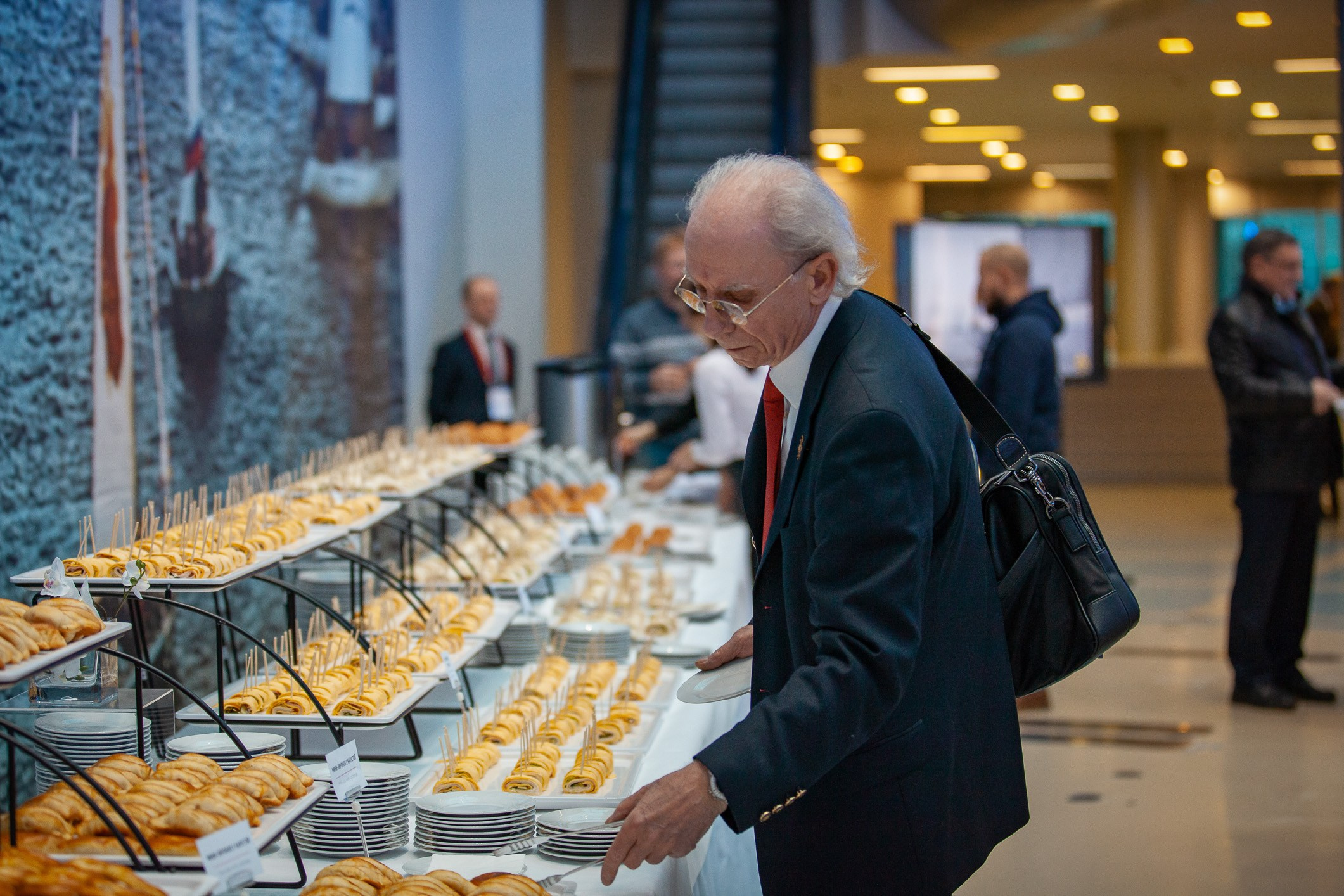 Гость мероприятия на фуршете. Пожилой мужчина в очках.
