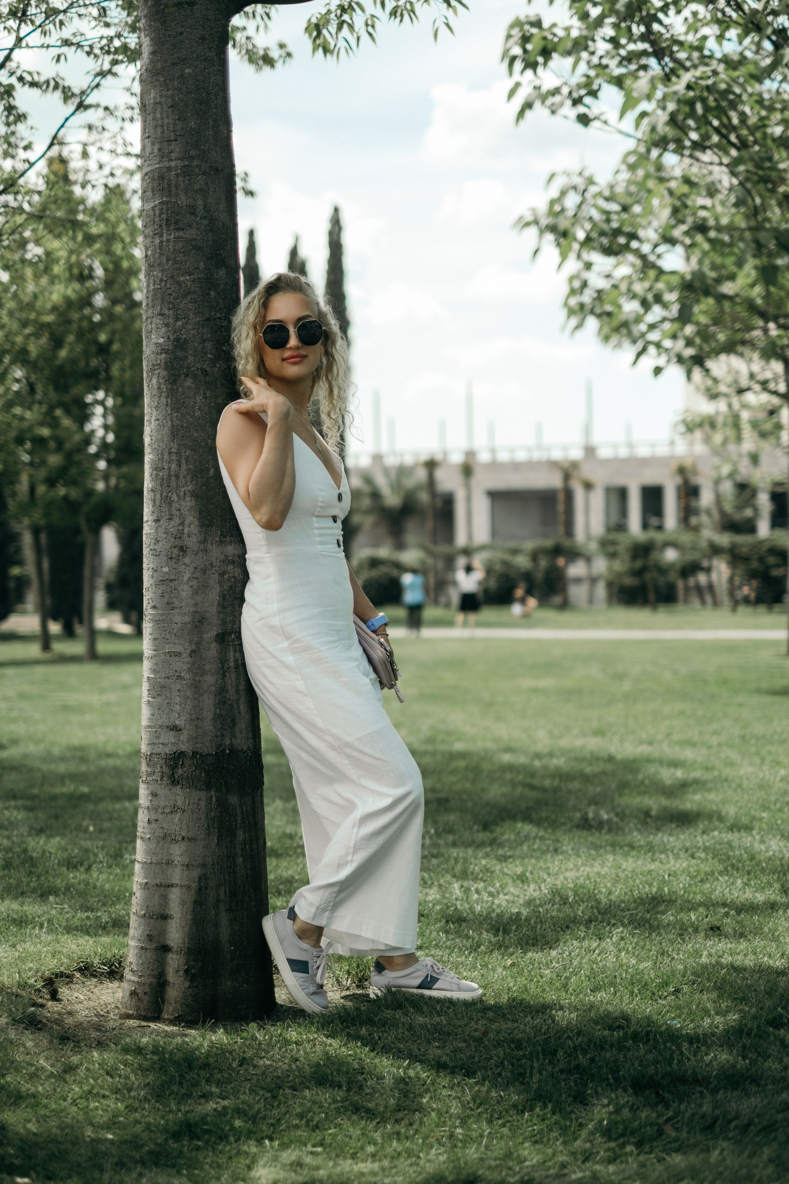 Девушка блондинка в белом длинном платье в парке Галицкого, Краснодар на фотосессии в черных очках Vouge на фоне залени и цветов