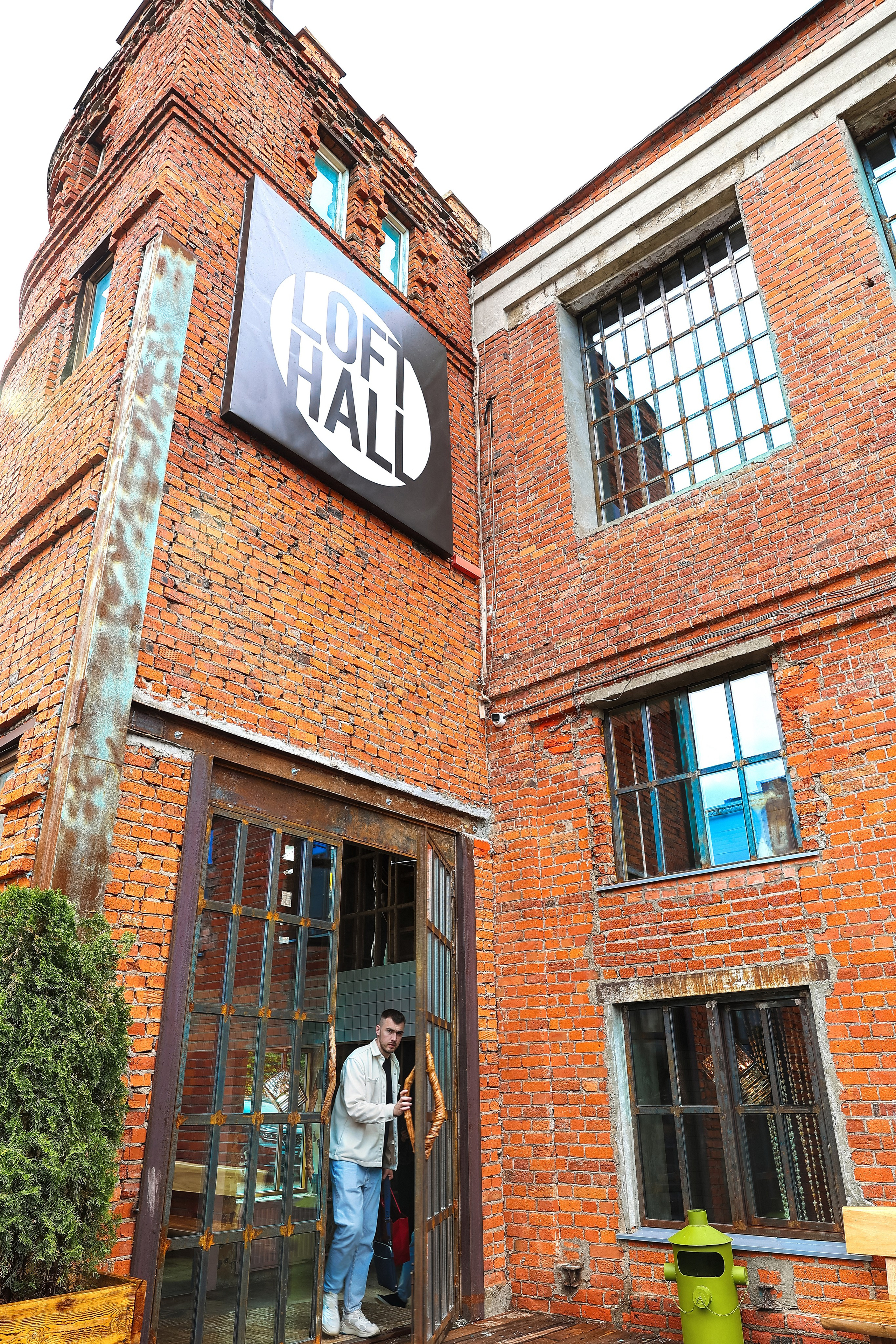 Входная группа LoftHall с массивными дверями и окном сверху, гость выходит из лофта во время события, фото с низкого ракурса.