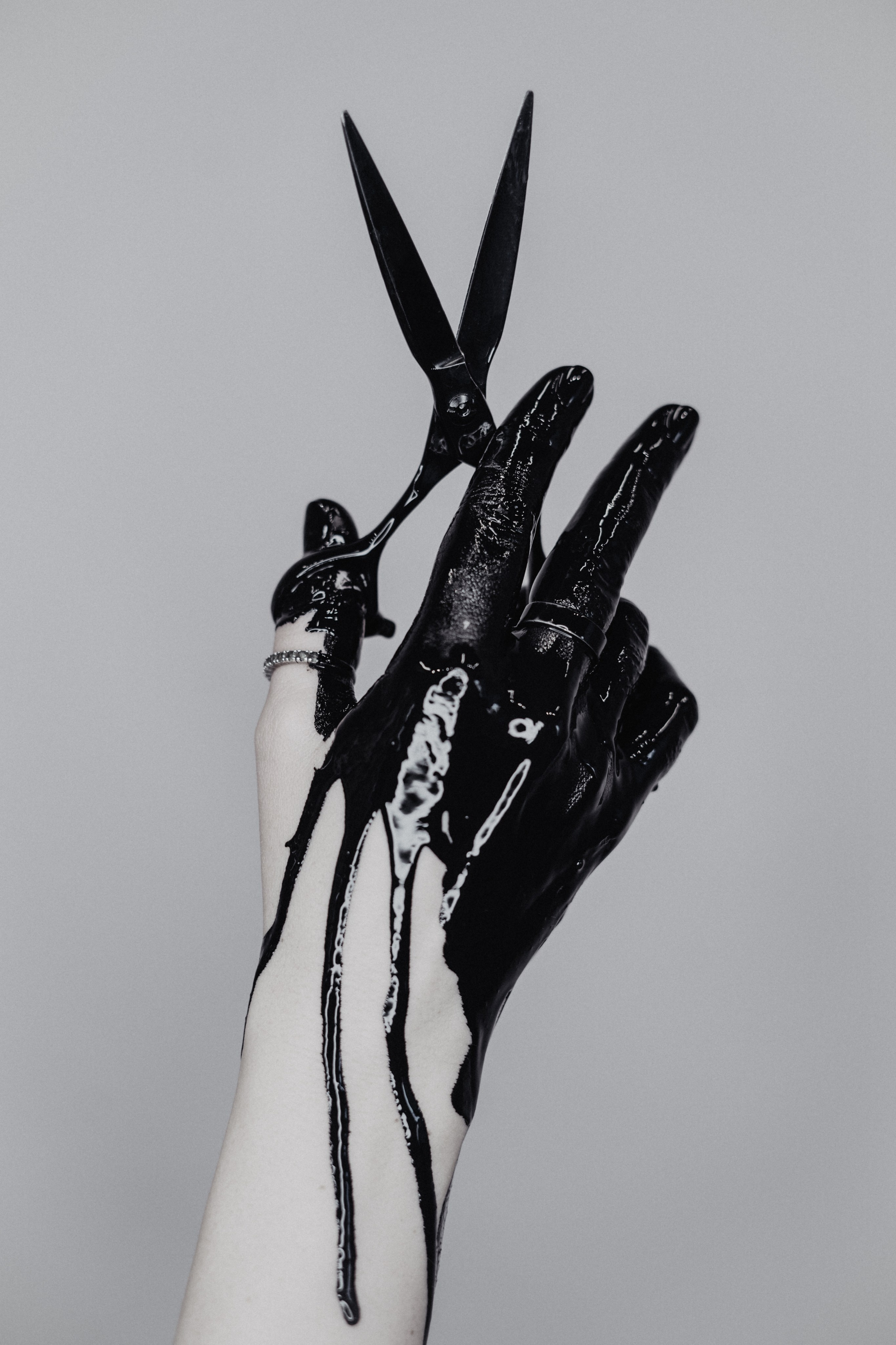 Conceptual portrait: a hand dripping with black paint holding scissors, black and white. Photo: Anna Ulianova