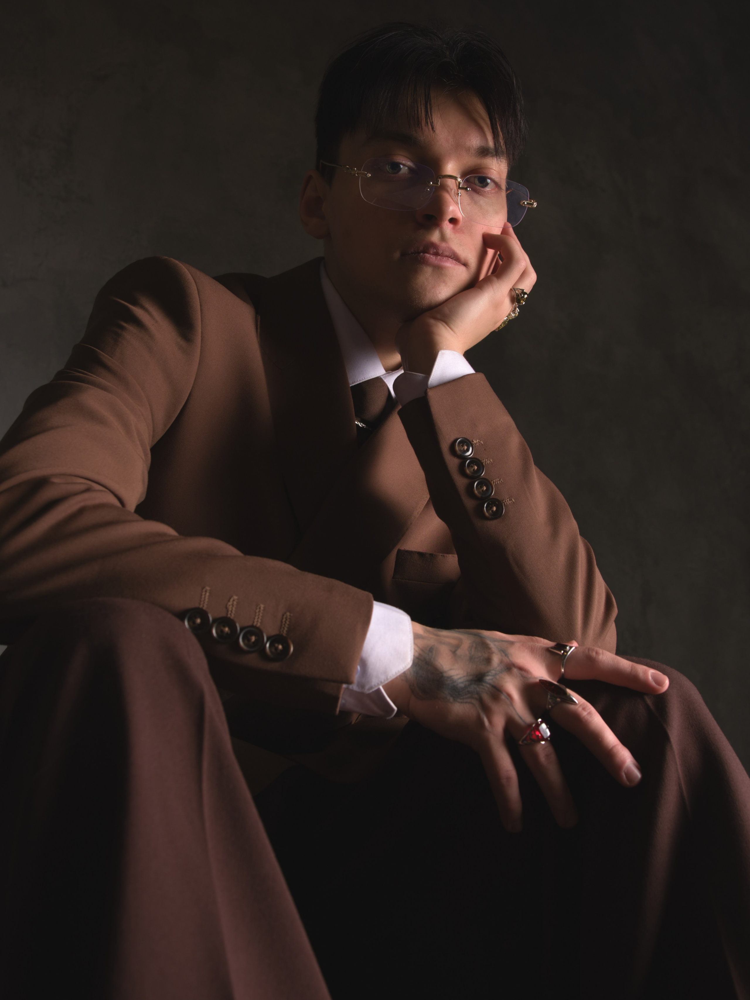 молодой мужчина в экстравагантном костюме сидит и смотрит в камеру