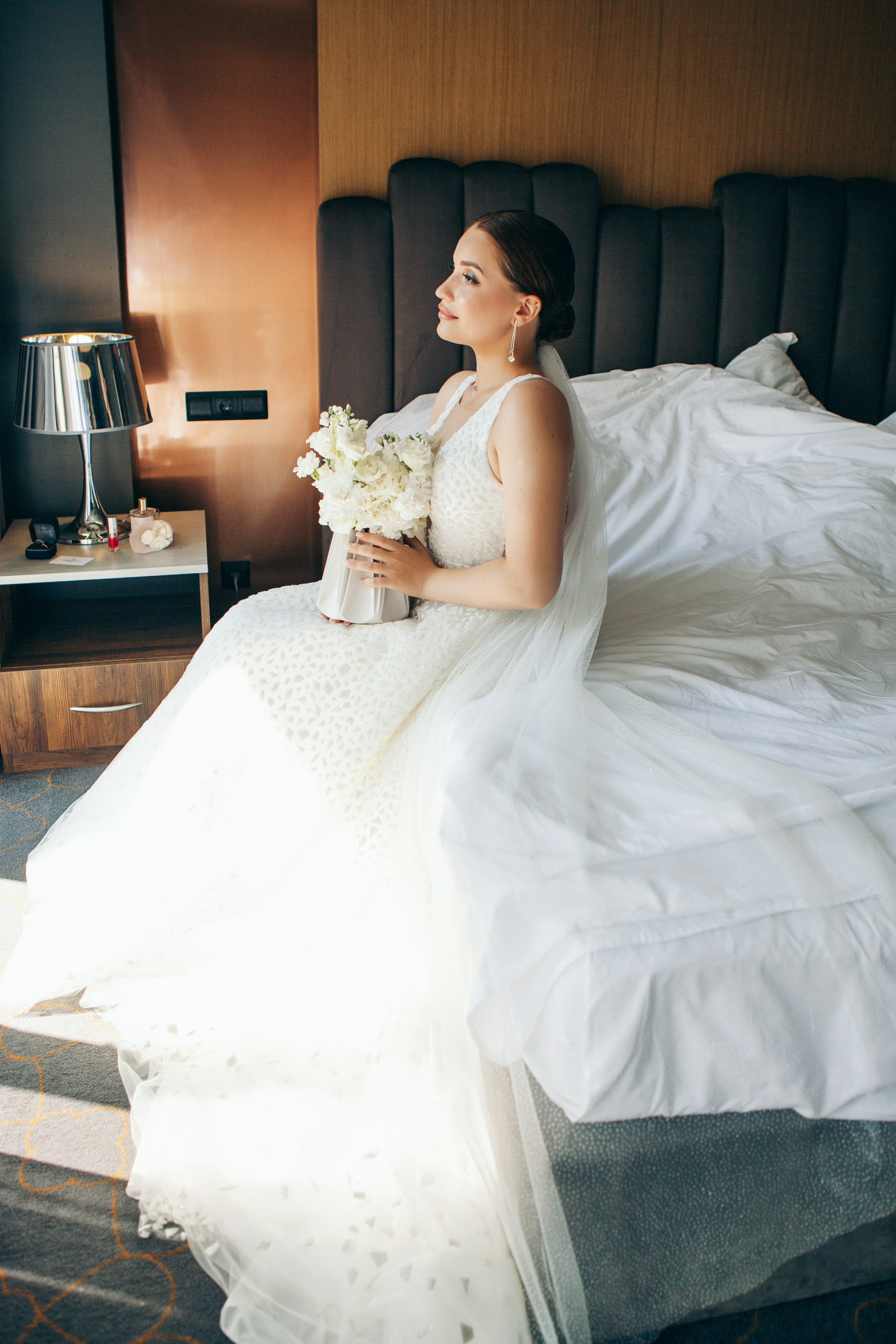 невеста сидит на кровати в платье и держит букет в руках, в ожидании жениха