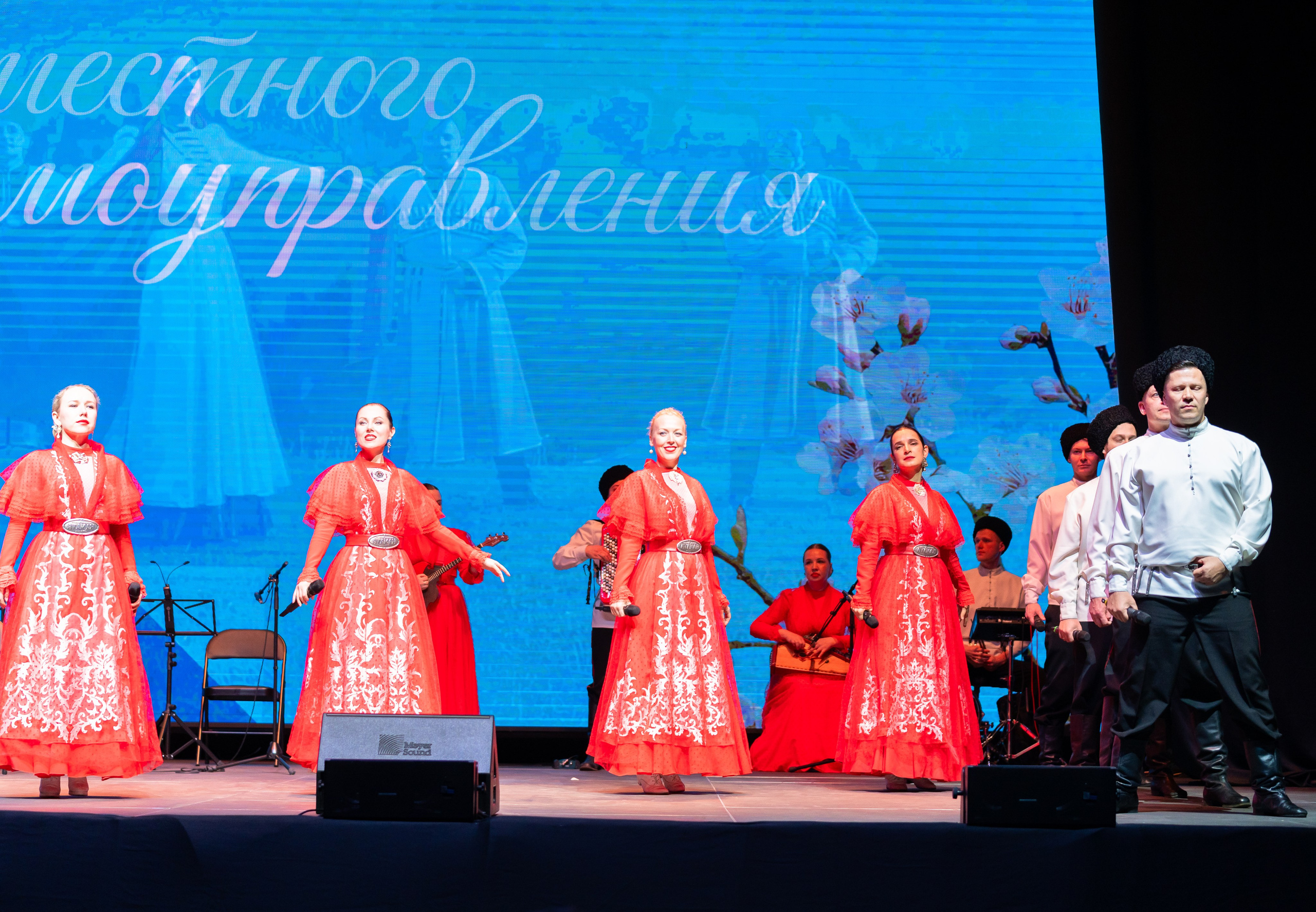 Ансамбль в красных народных костюмах на сцене во время концерта, посвящённого Дню местного самоуправления Санкт-Петербурга 2026. Фотограф Евгений Мальцев.