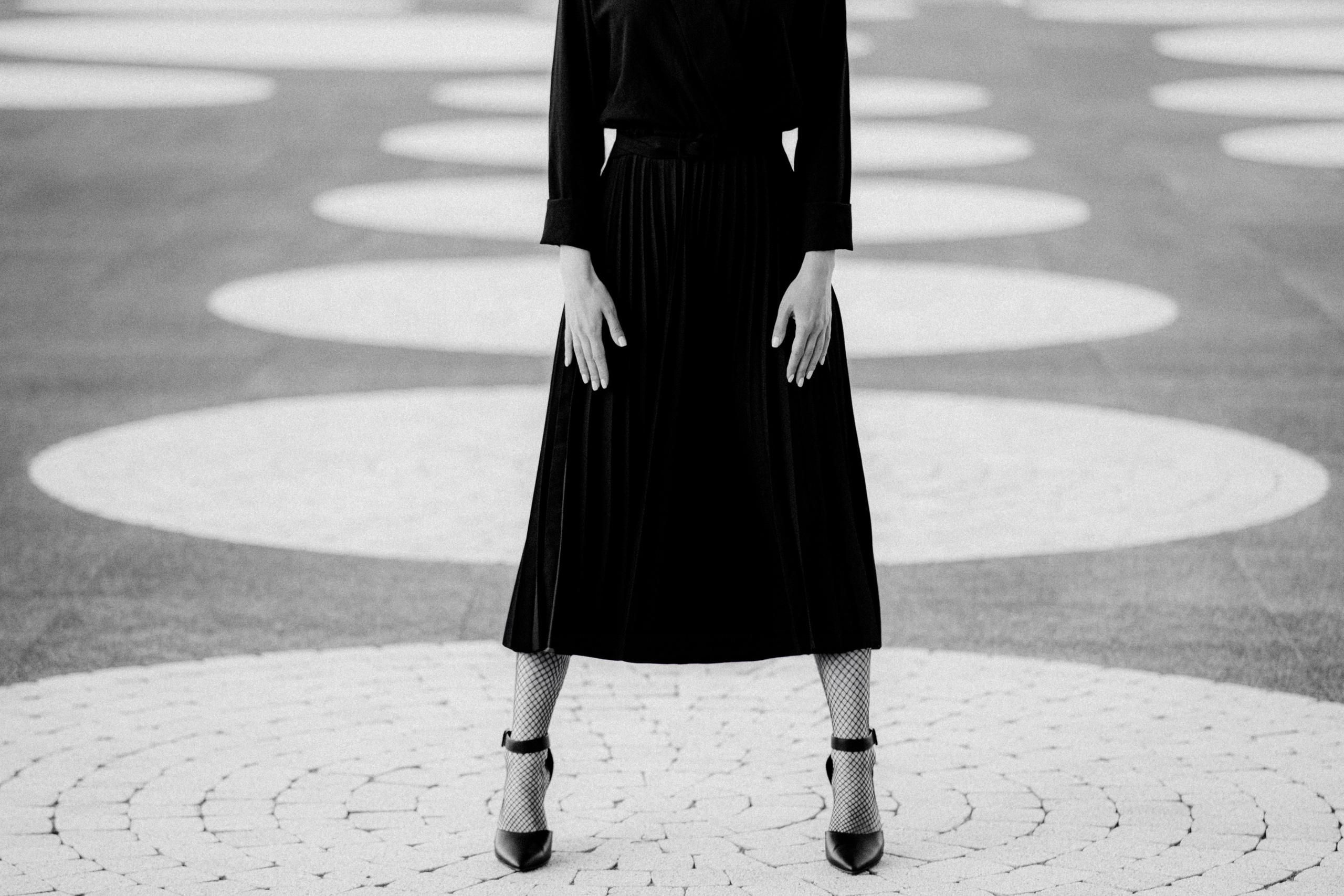 Женщина в чёрной юбке и туфлях на каблуках стоит на фоне графичных кругов, чёрно-белая минималистичная фотосъёмка