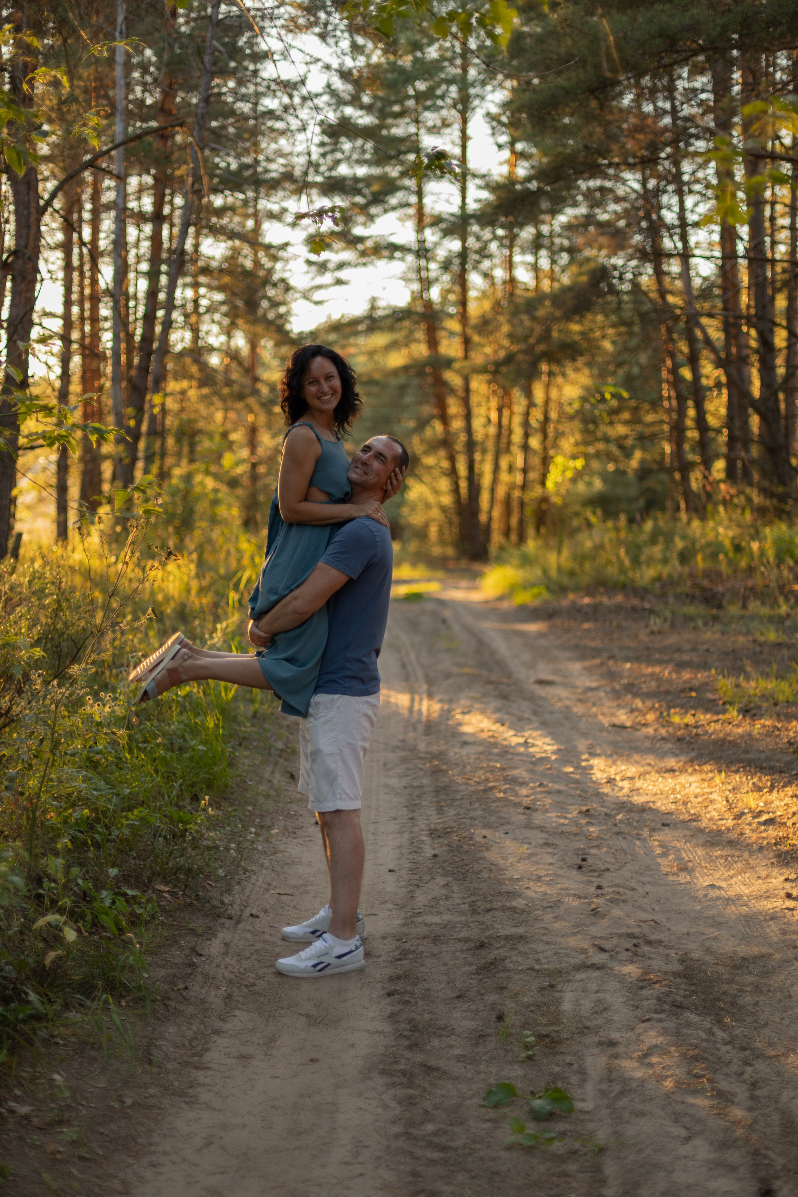 Фотосессия пары в сосновом лесу летом на закате, мужчина держит девушку на руках