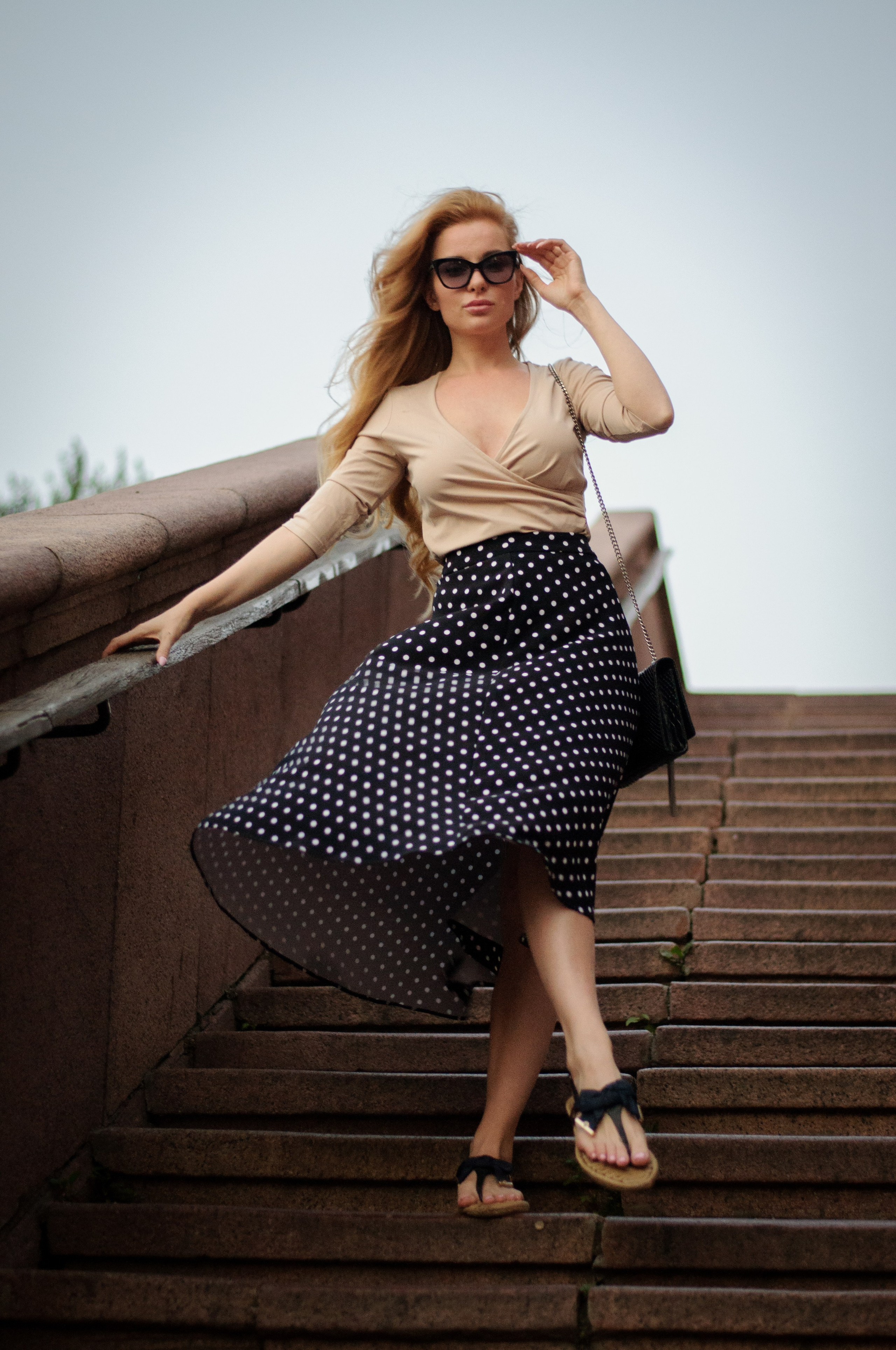 девушка в юбке стоит на лестнице и ветер играет с подолом юбки