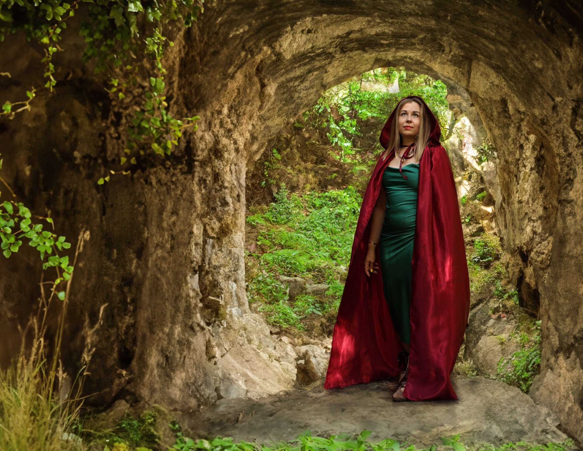 девушка в красном плаще стоит в каменной пещере на тематической фотосессии