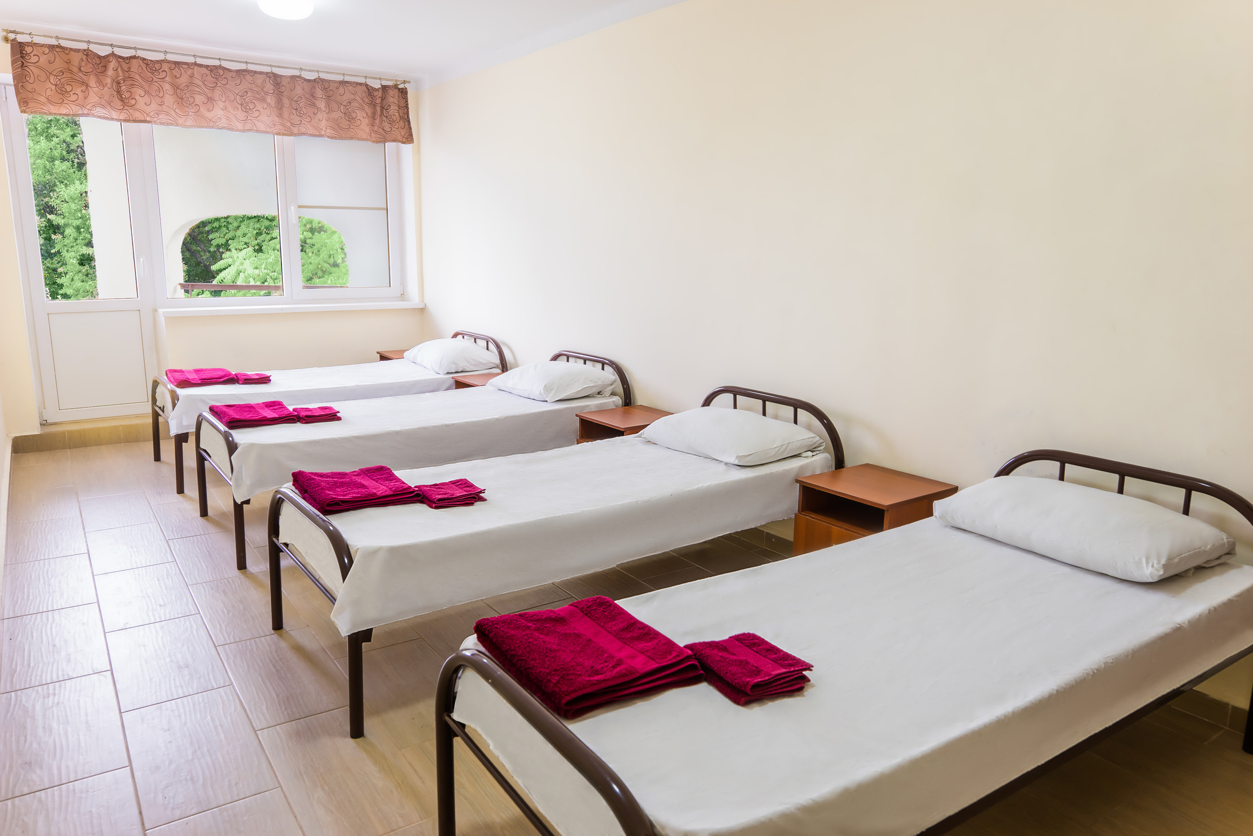 Комната в жилом корпусе, четыре кровати, шкаф для одежды, тумбочка у каждой кровати, вид на зеленую зону