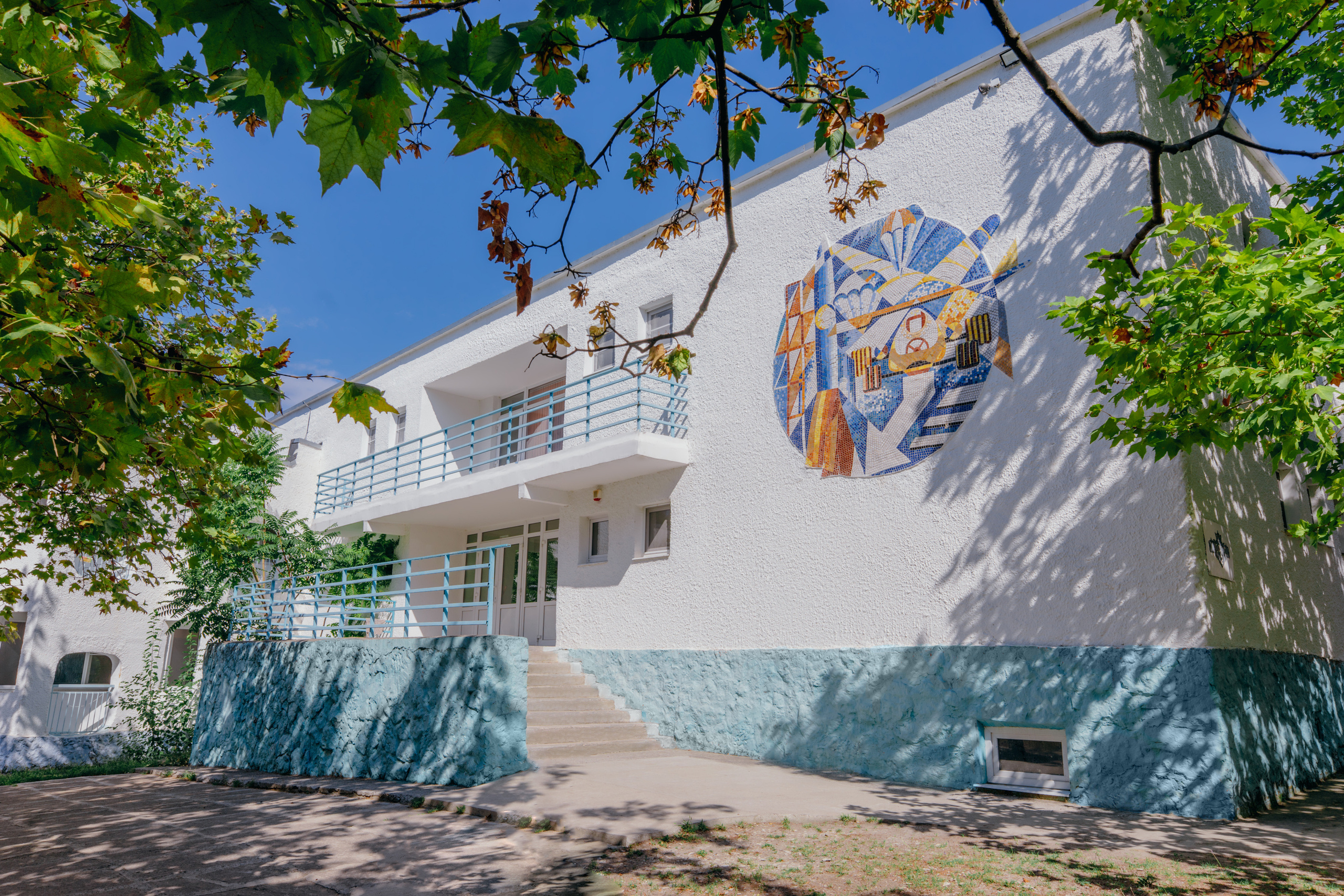 Двухэтажный корпус Фрегат, вокруг много зелени, мозаика на здании