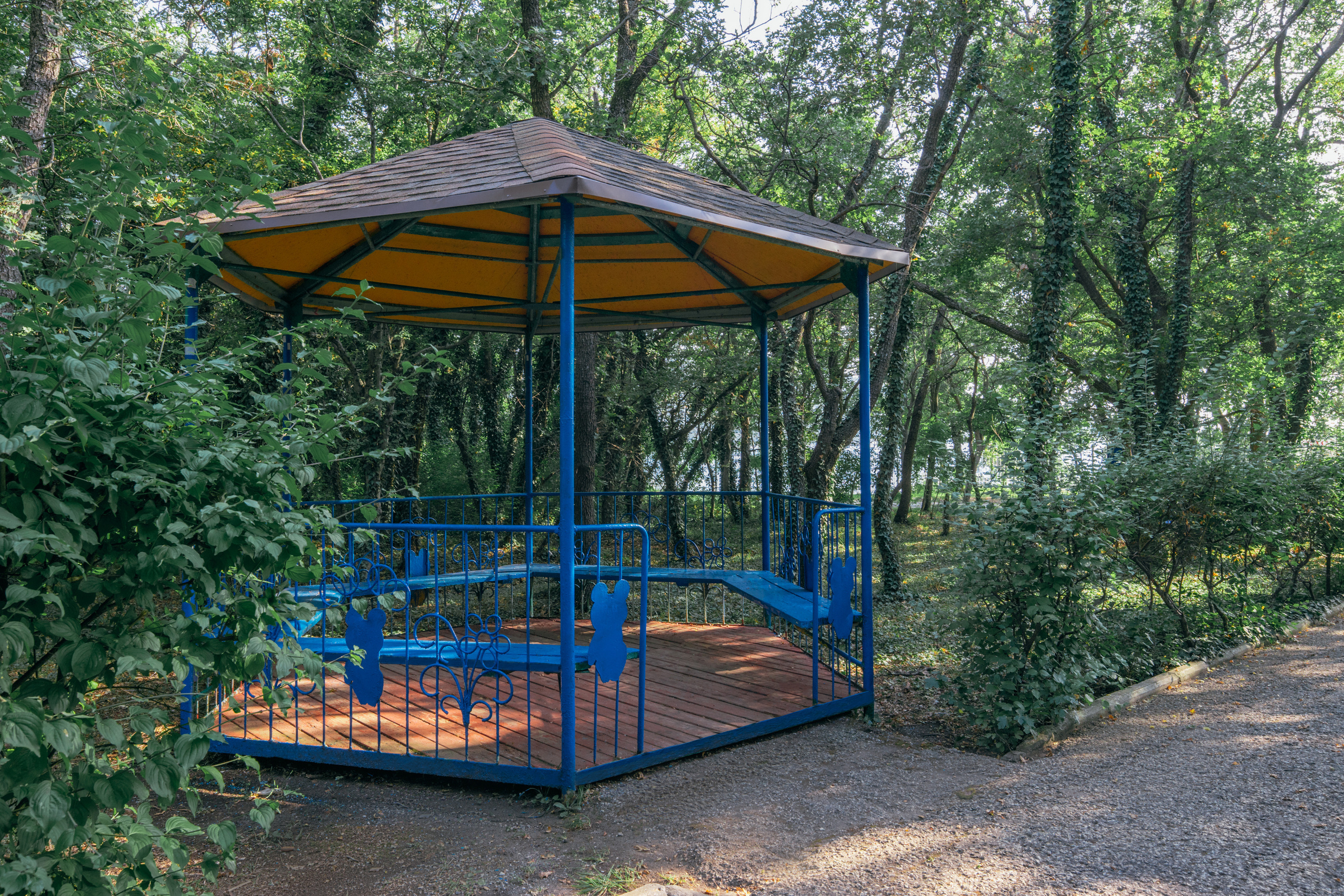 Беседка для отдыха, расположенная в тени деревьев, с крытой крышей.