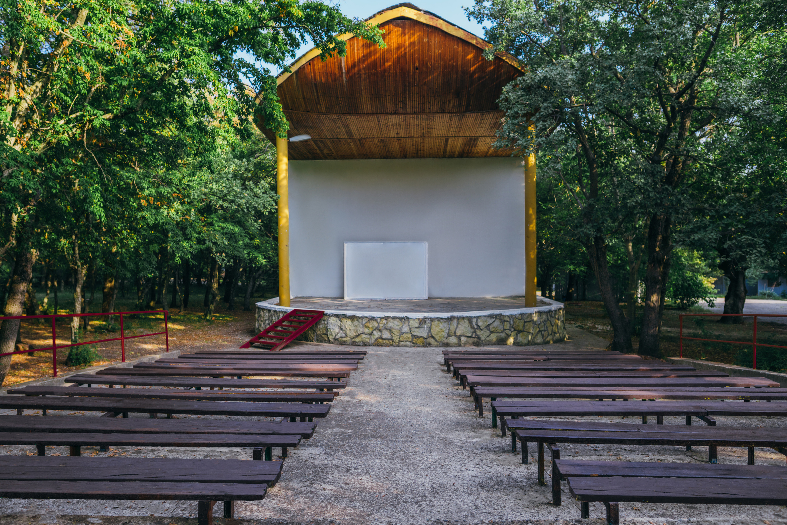 Летняя эстрада со сценой, скамейками для зрителей на переднем плане.