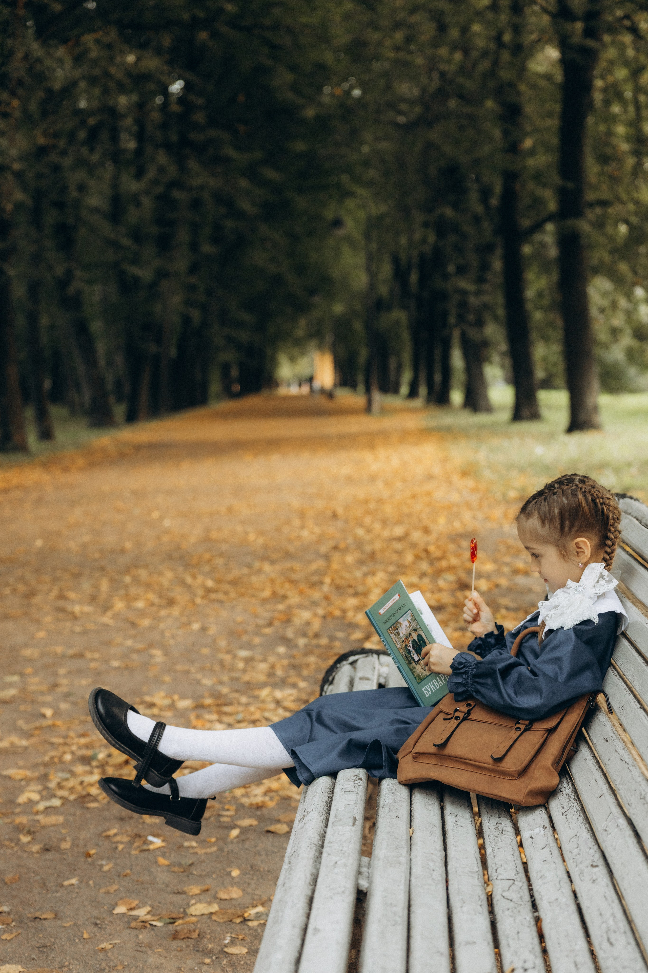 фотография первоклашки, которая сидит на скамейке и читает букварь