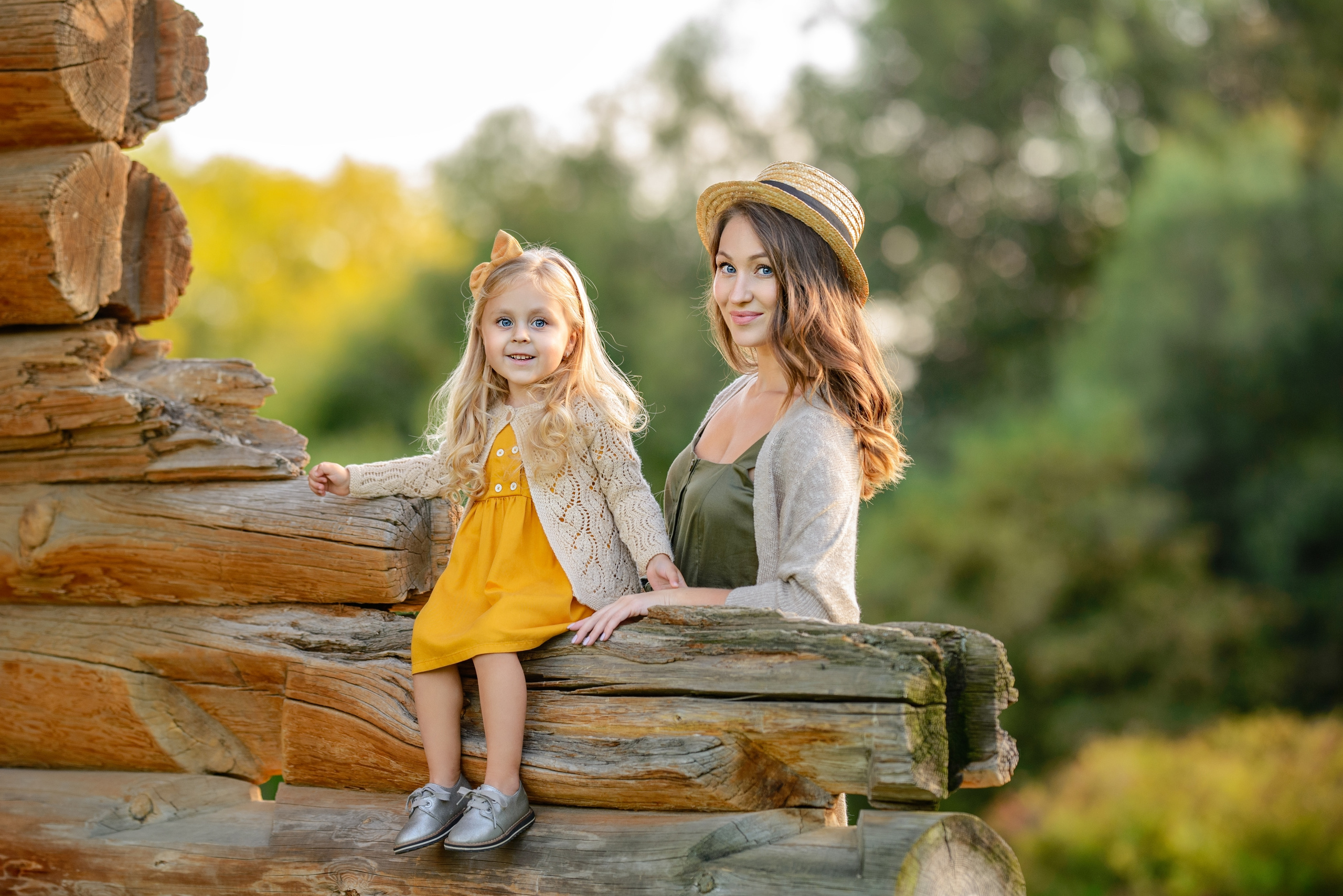 Девочка сидит на бревне, мама стоит рядом.