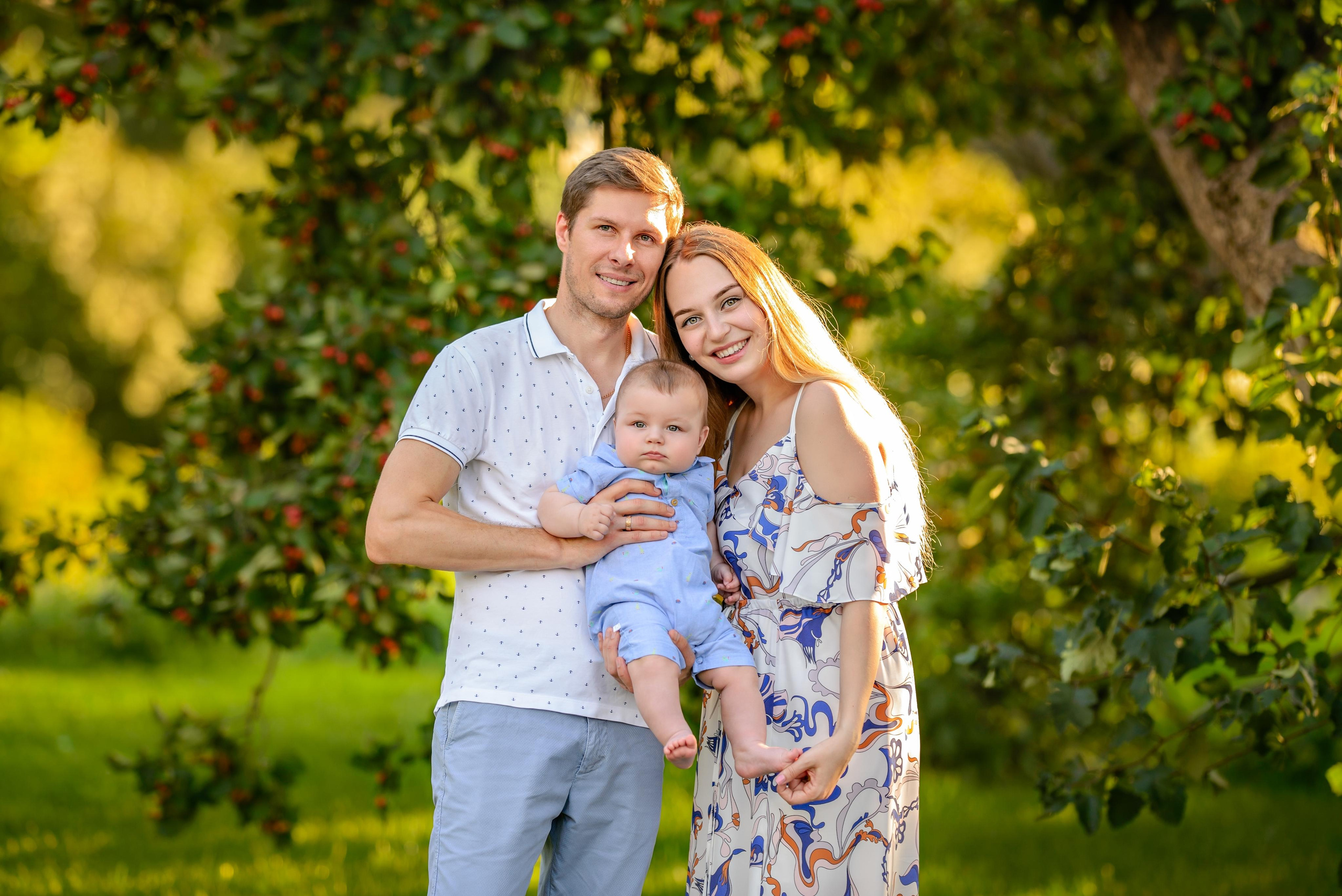 Семья гуляет в парке, мама склонила голову на плечо папе, на руках у них малыш