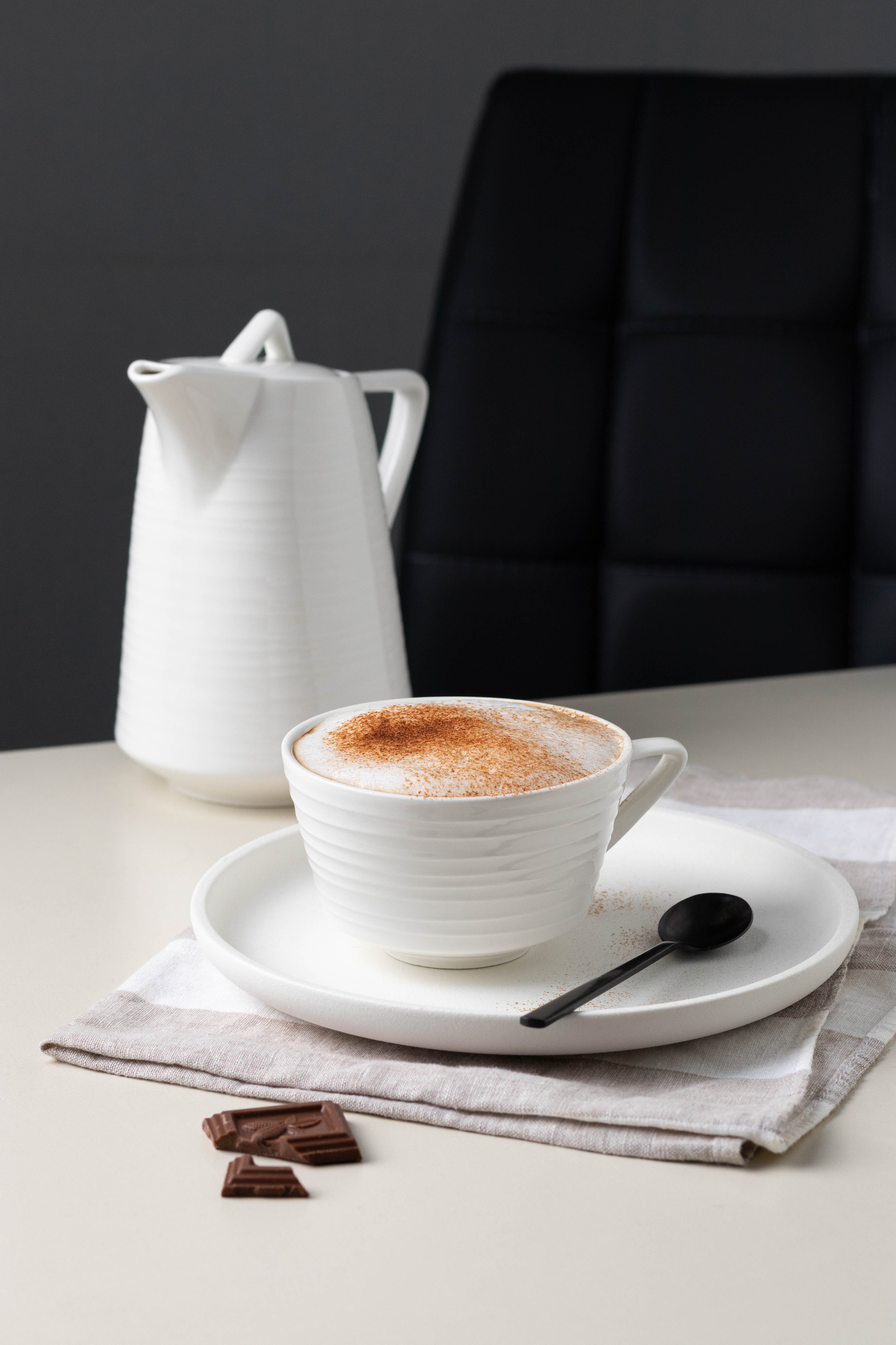 Чашка капучино с корицей с кофейником и долькой шоколада, деловой завтрак.