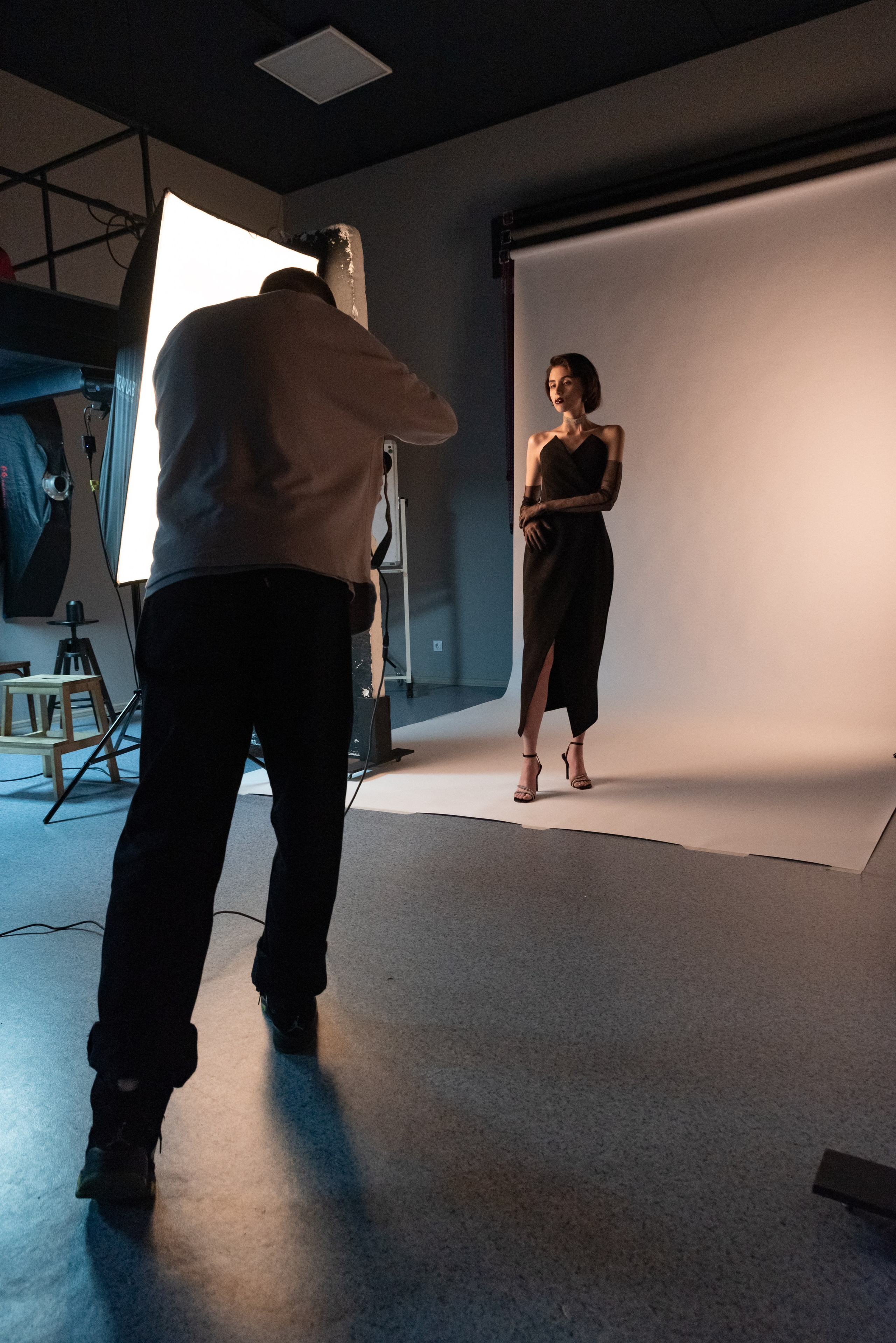 Фотограф снимает модель на белом фоне в студии. Сбоку большой источник света.