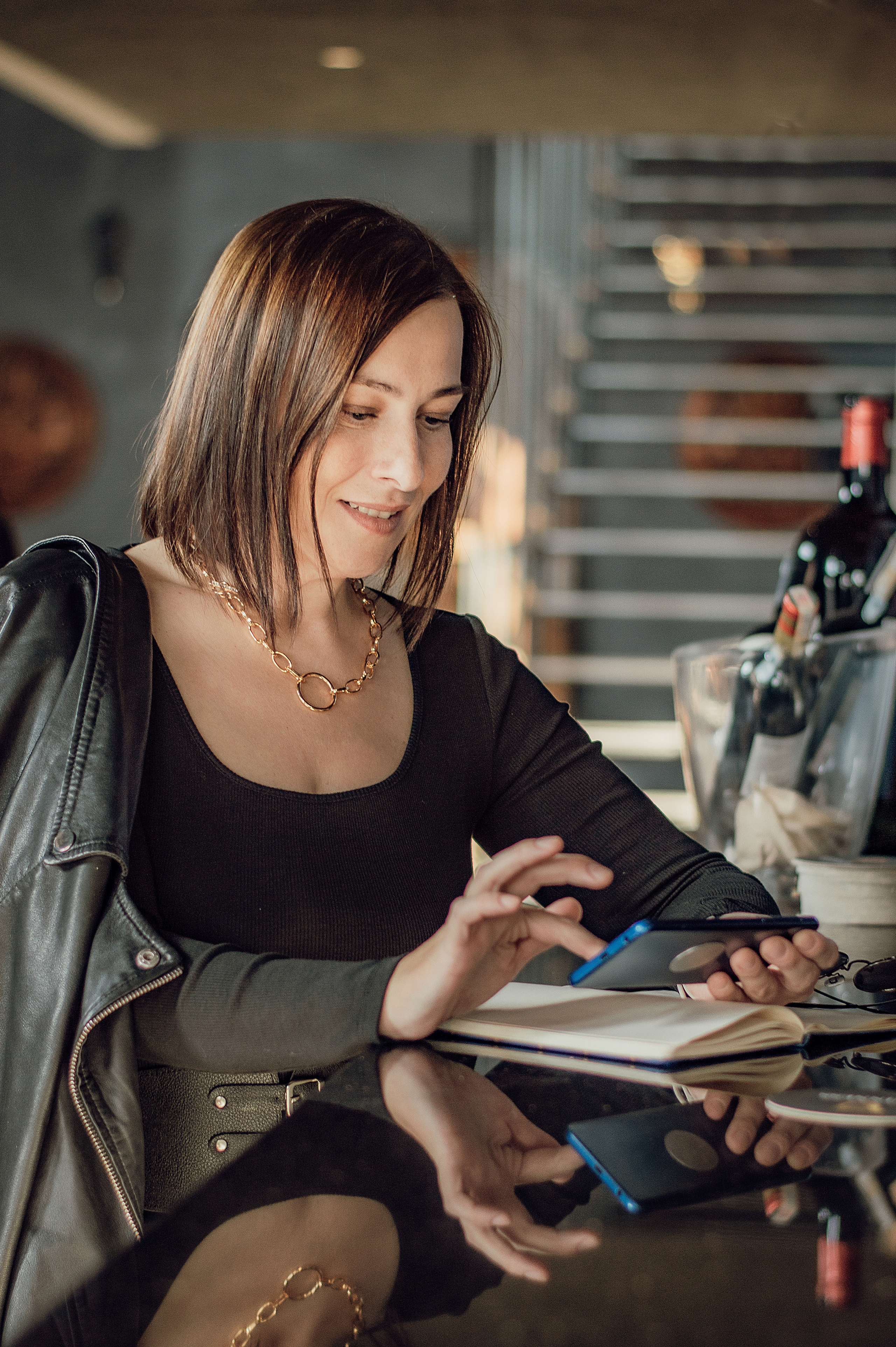 девушка бухгалтер экономист бизнес леди в кафе смотрит в телефон куртка косуха кожаная